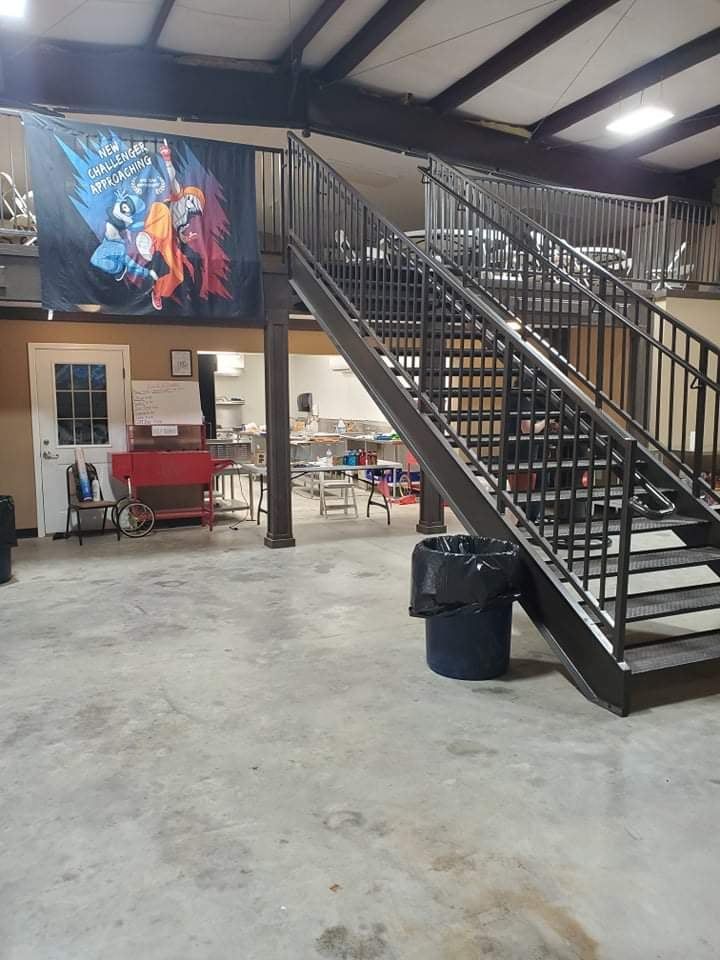 Interior with metal staircase, banner, tables, and trash can.