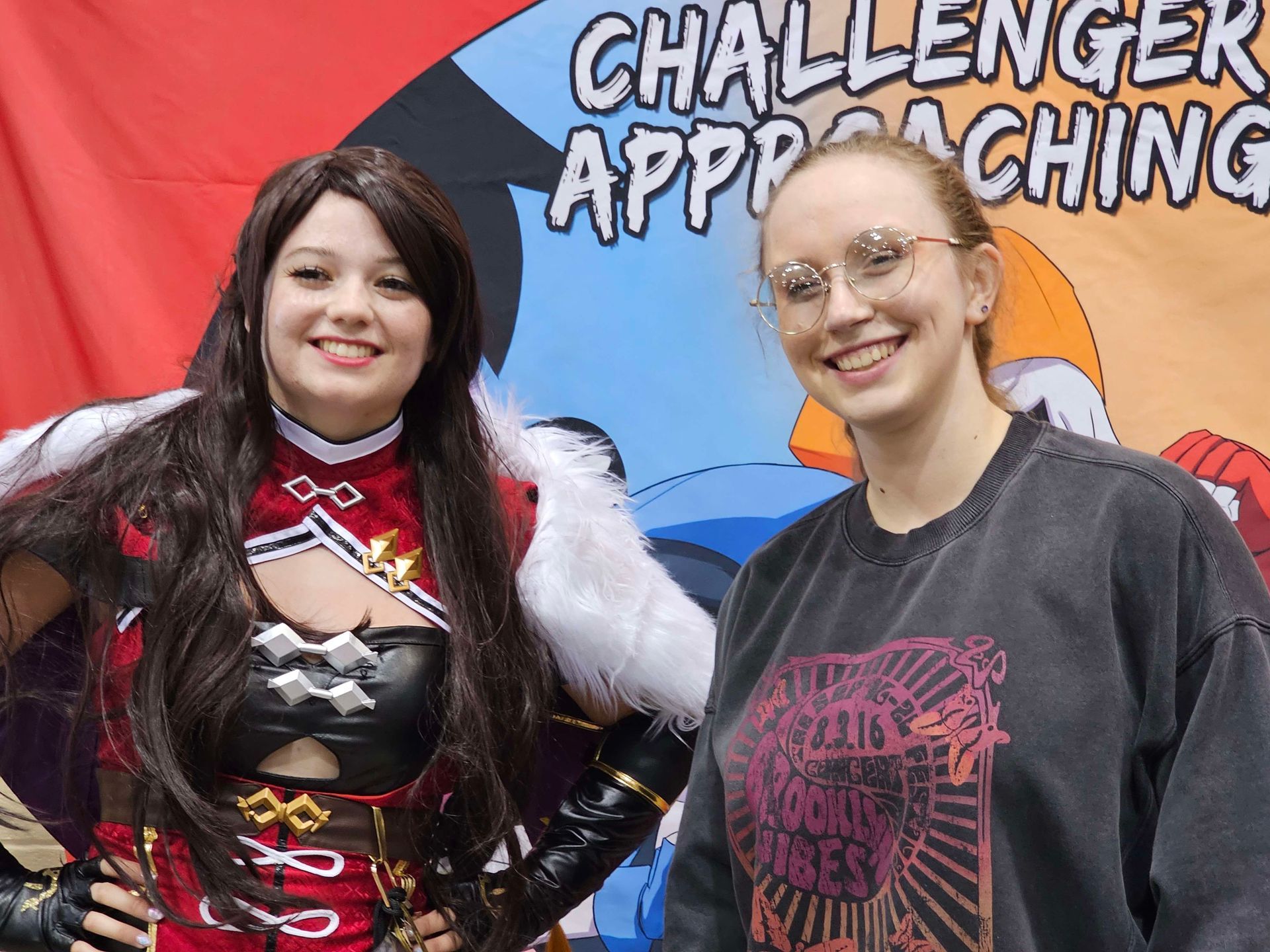 Woman in cosplay poses with another woman in front of a banner that says 
