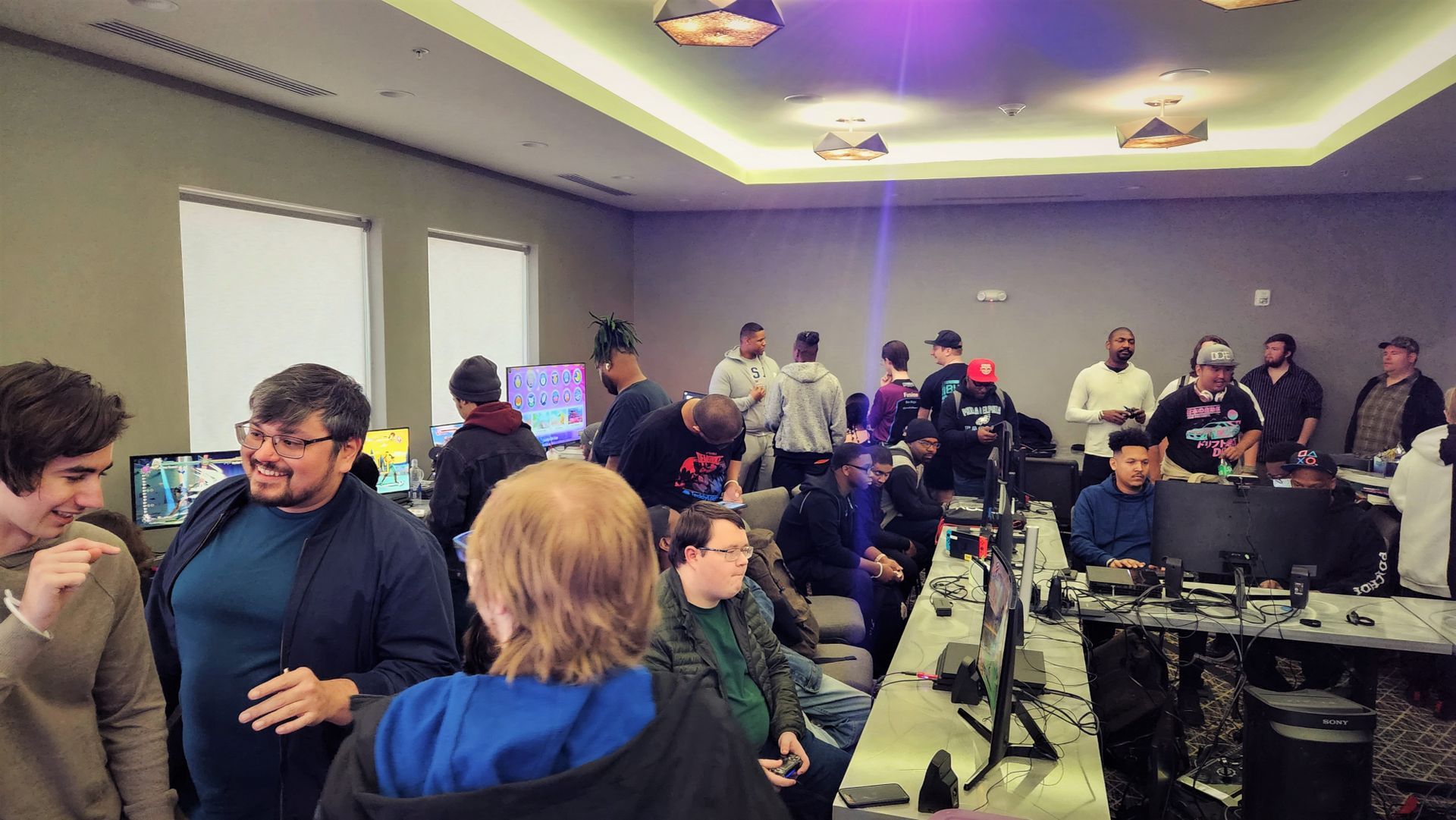 A crowded room with people gathered around computers. Some are interacting, others watching.