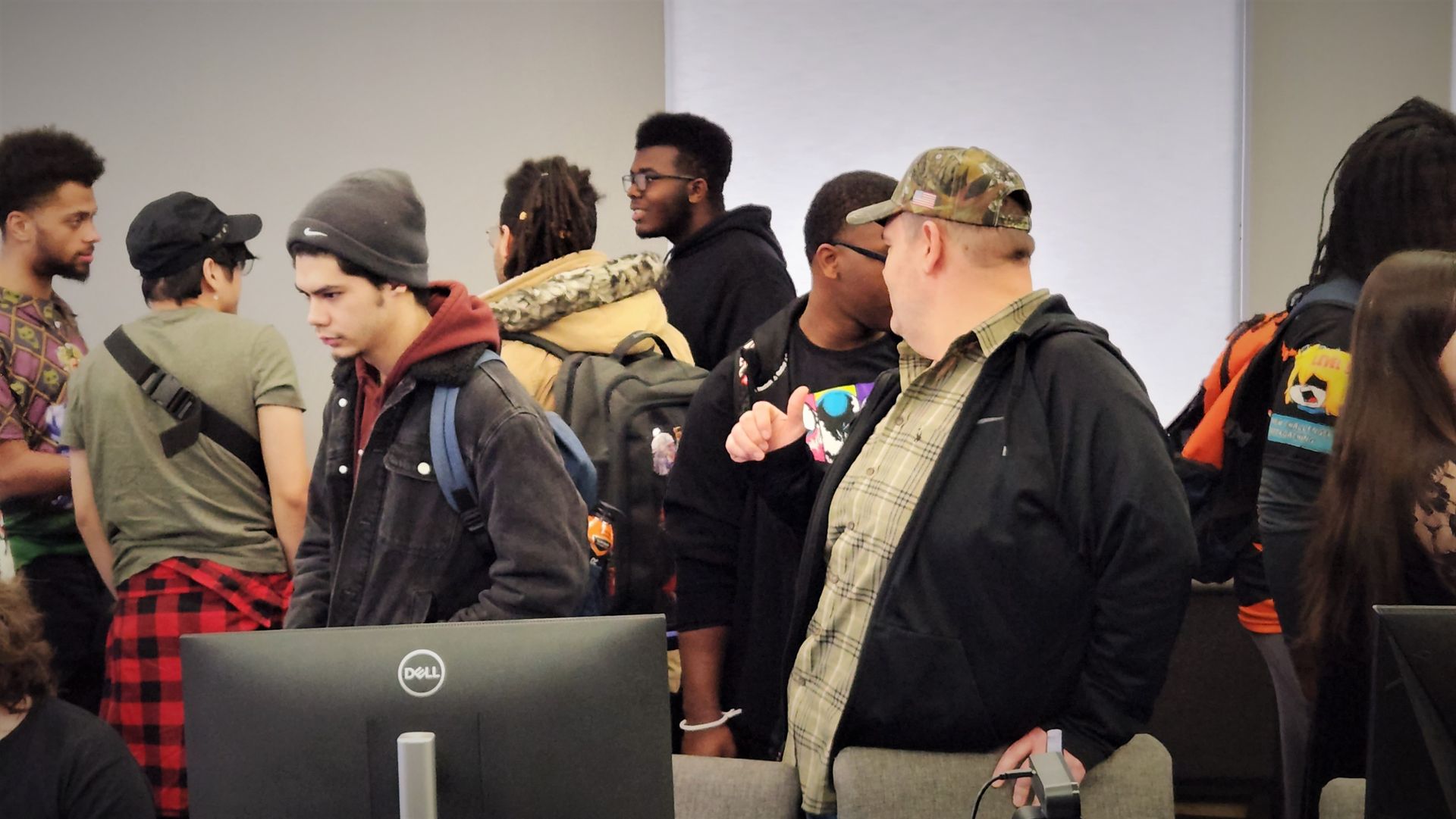 Group of people in a room with computers, some are talking, others look on.