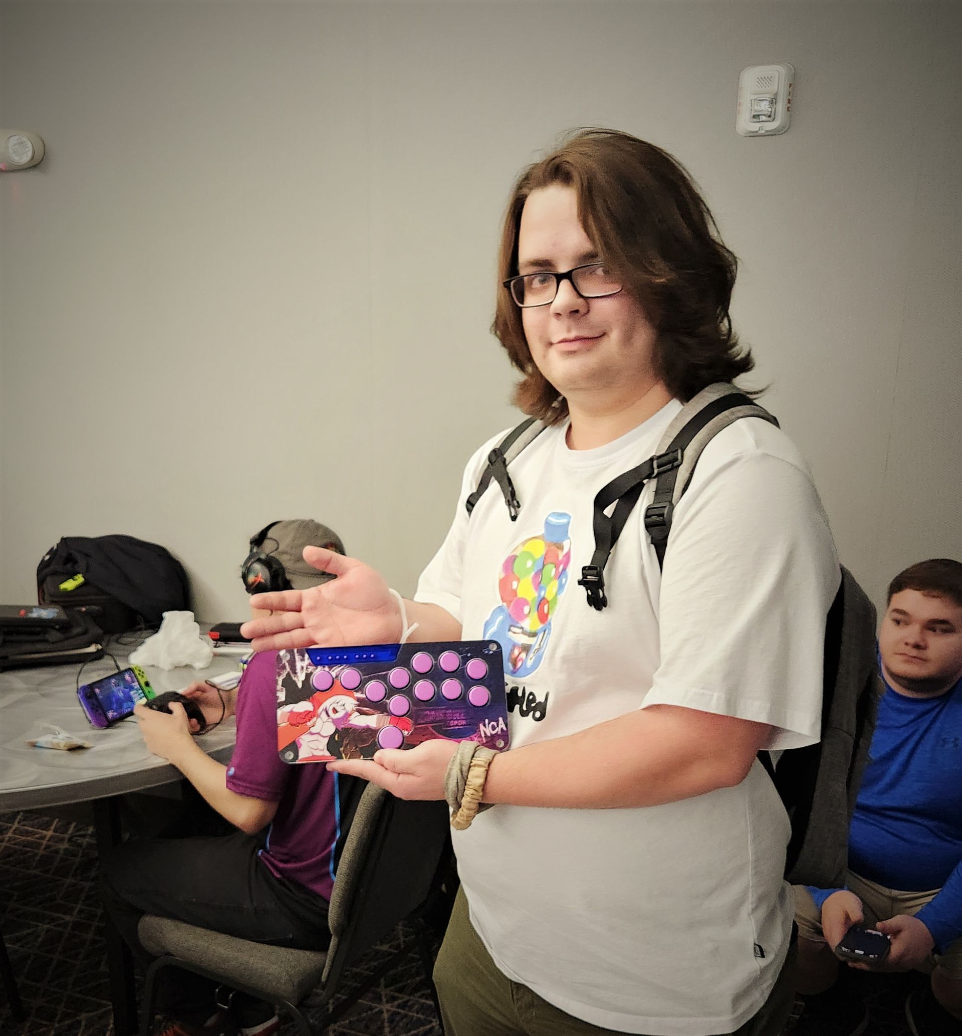 Man holding a tablet with artwork. He's smiling and pointing at the screen. People are visible in the background.