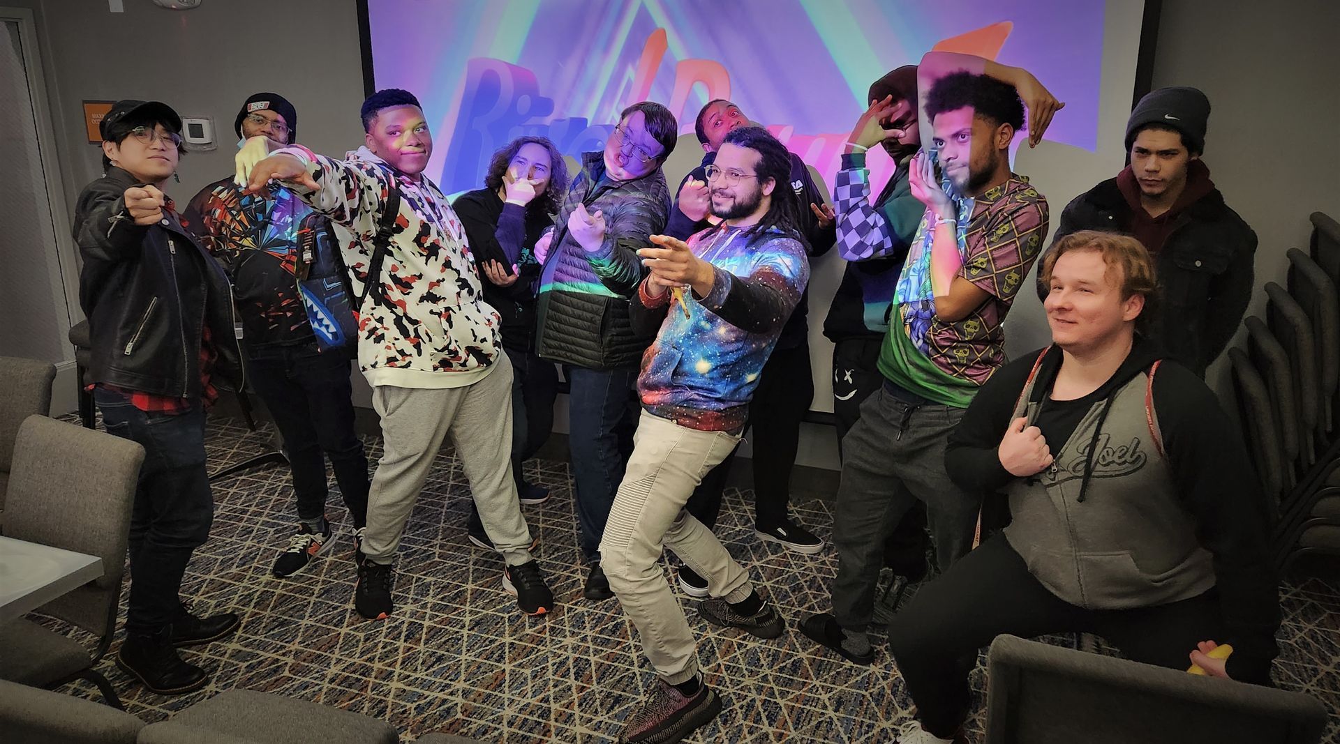 Group of people posing with arms up, in front of a colorful backdrop in a room.