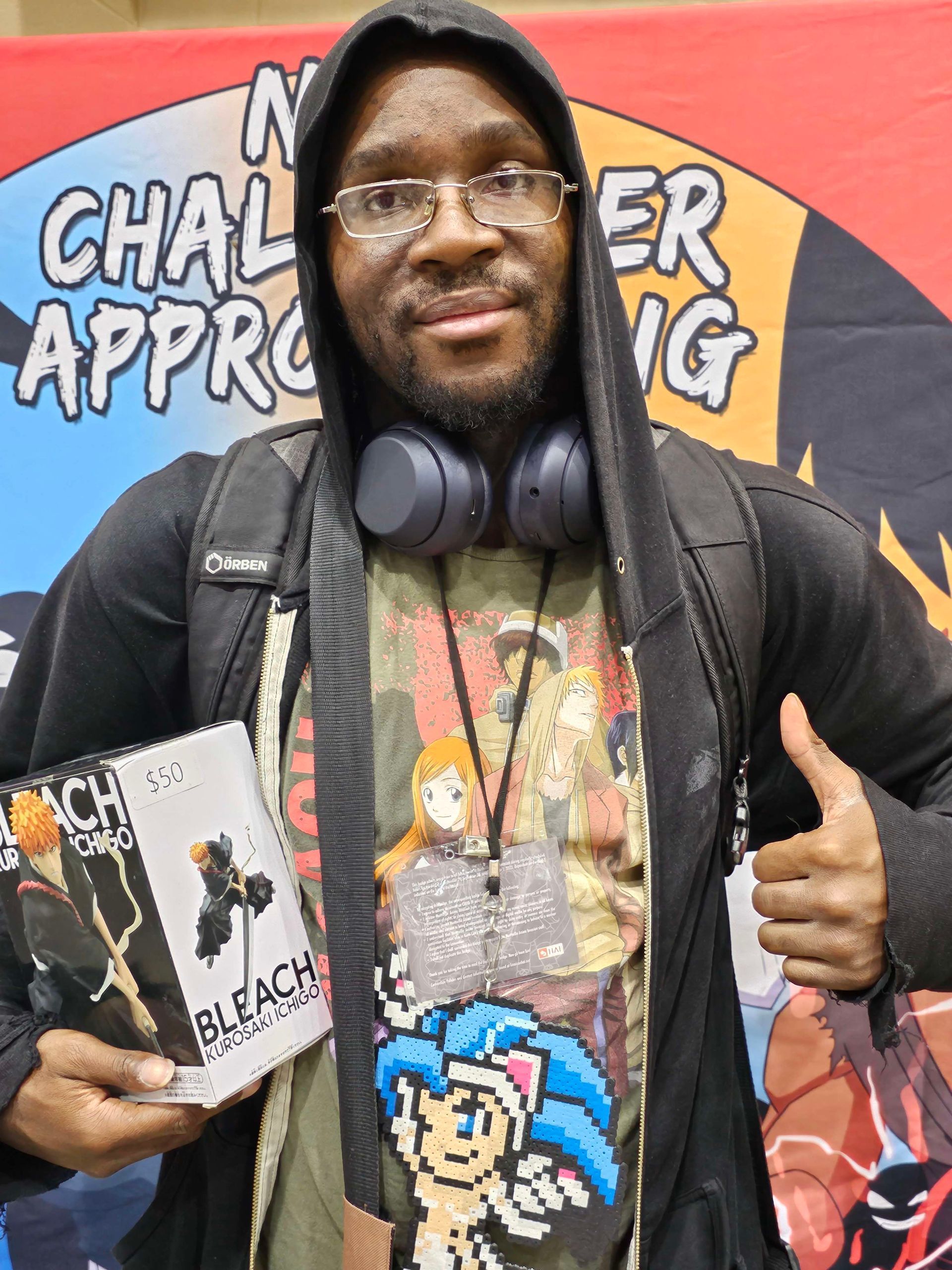 Person holding Bleach manga, wearing a hoodie, and giving a thumbs up. A colorful fan poster in the background.