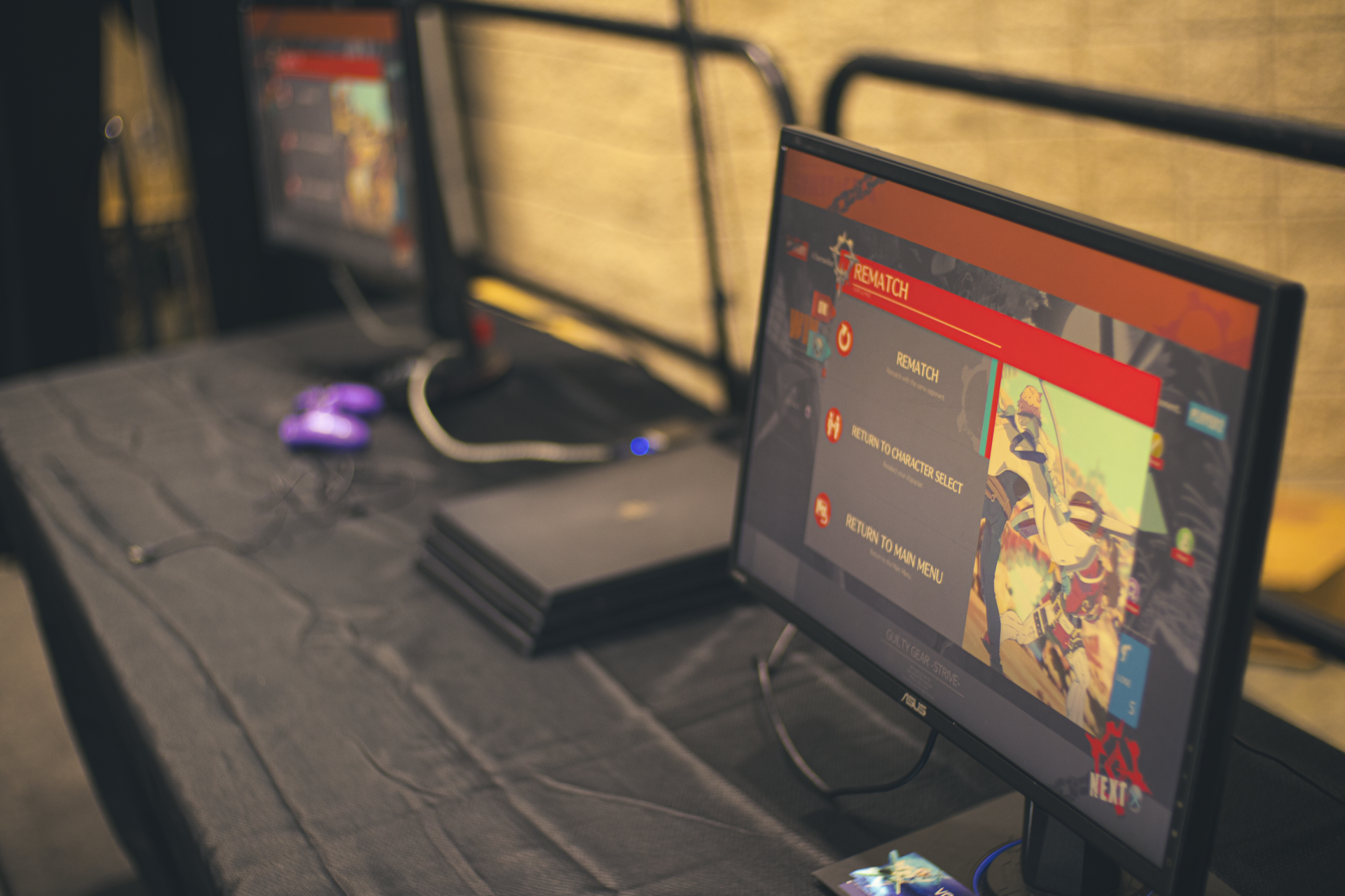 Gaming setup with two monitors showing a game menu, a console, and a gamepad on a black table.