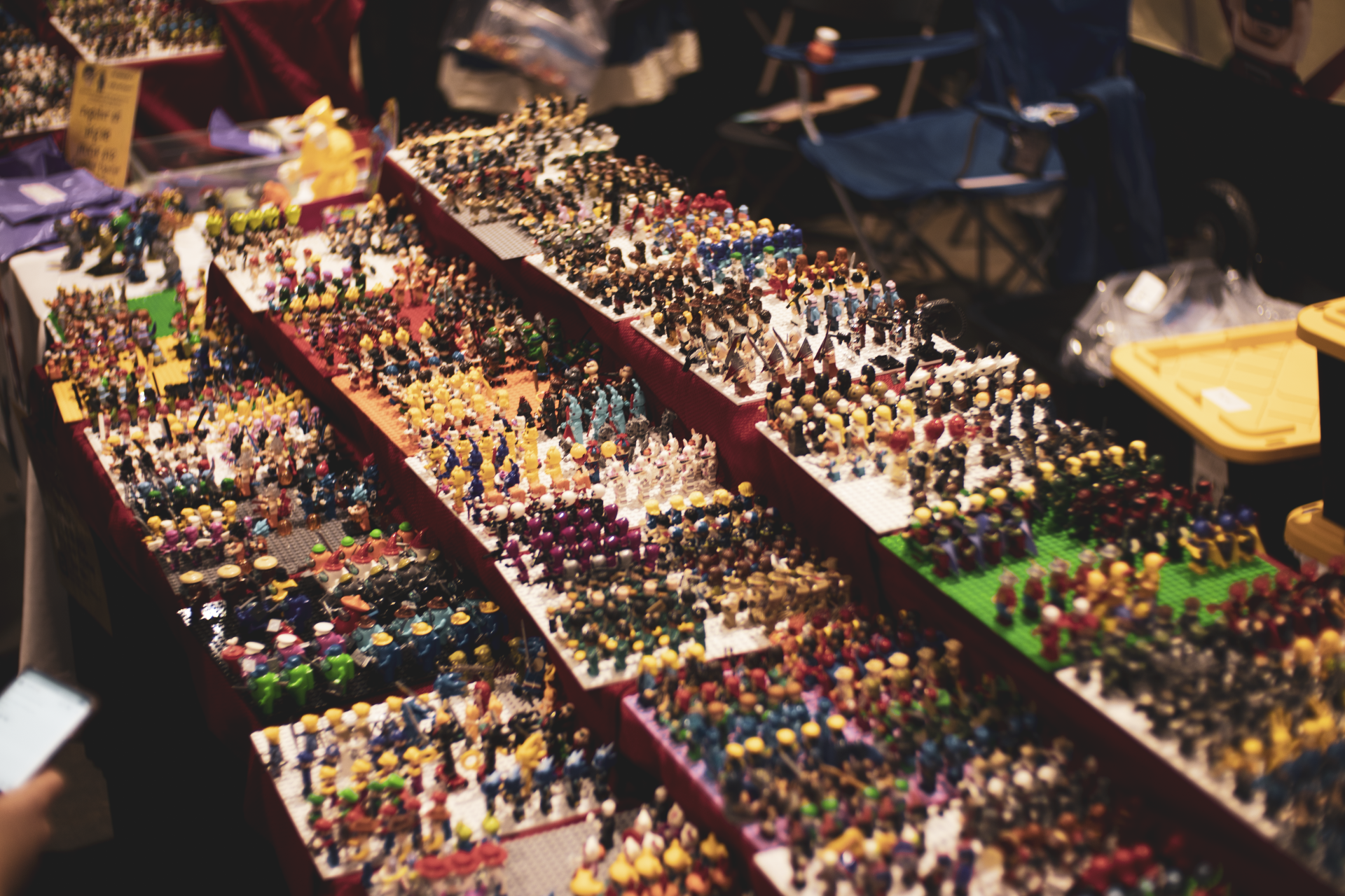 Lego figurines displayed on tiered shelves at a market. Numerous colorful figures fill the stands.