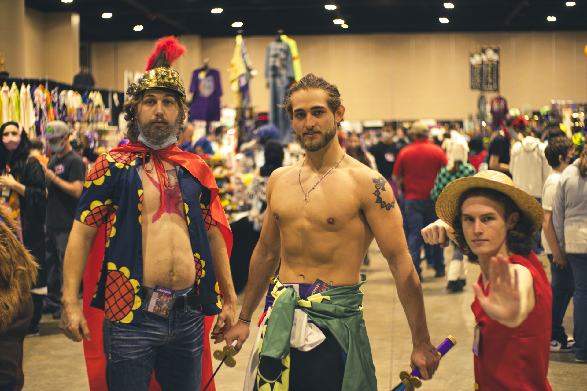 Three cosplayers at an event, dressed as anime characters, hold swords and pose for a photo.