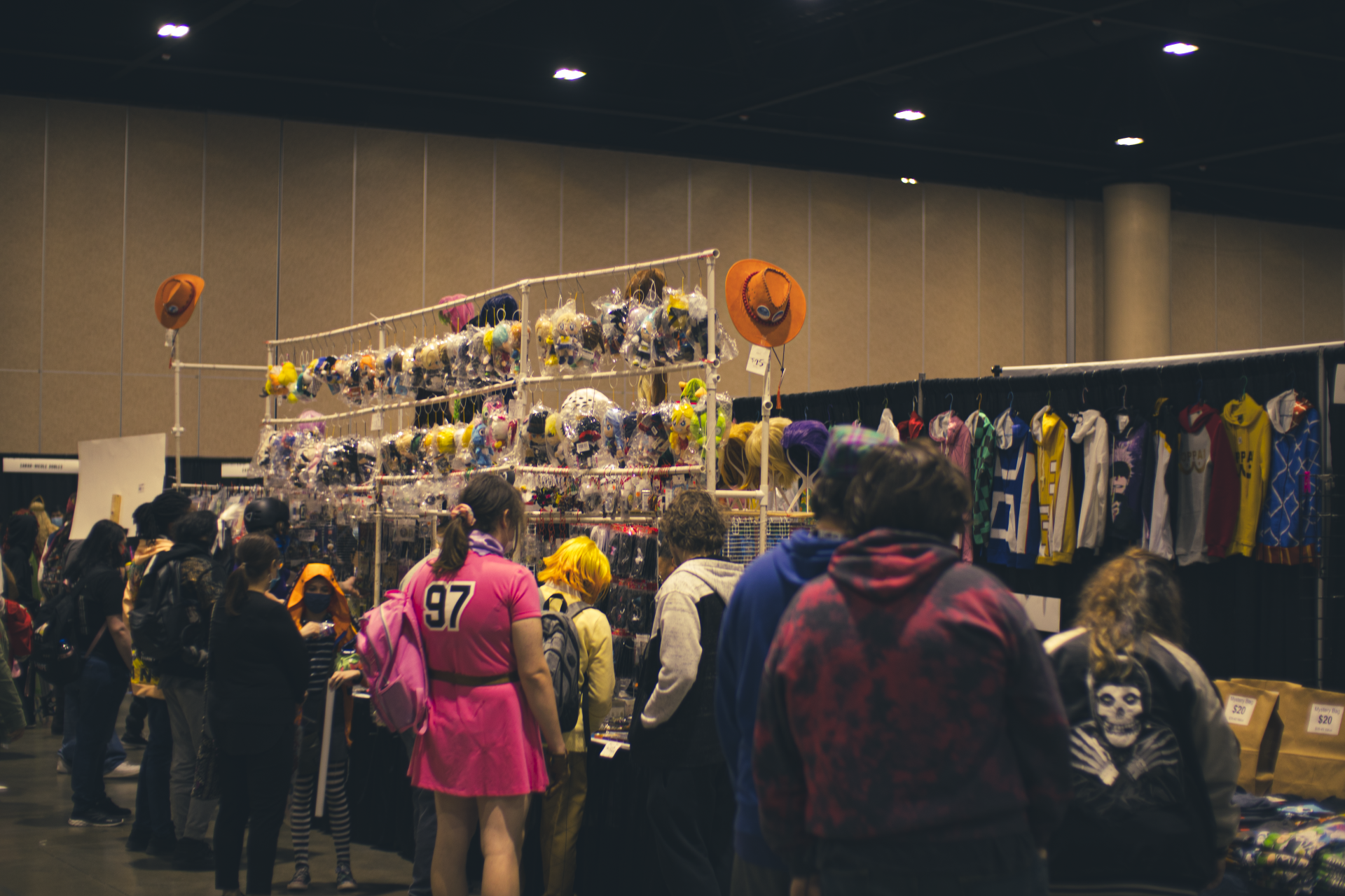 Convention attendees browsing a vendor booth with accessories and clothing. Halloween decorations hang above.