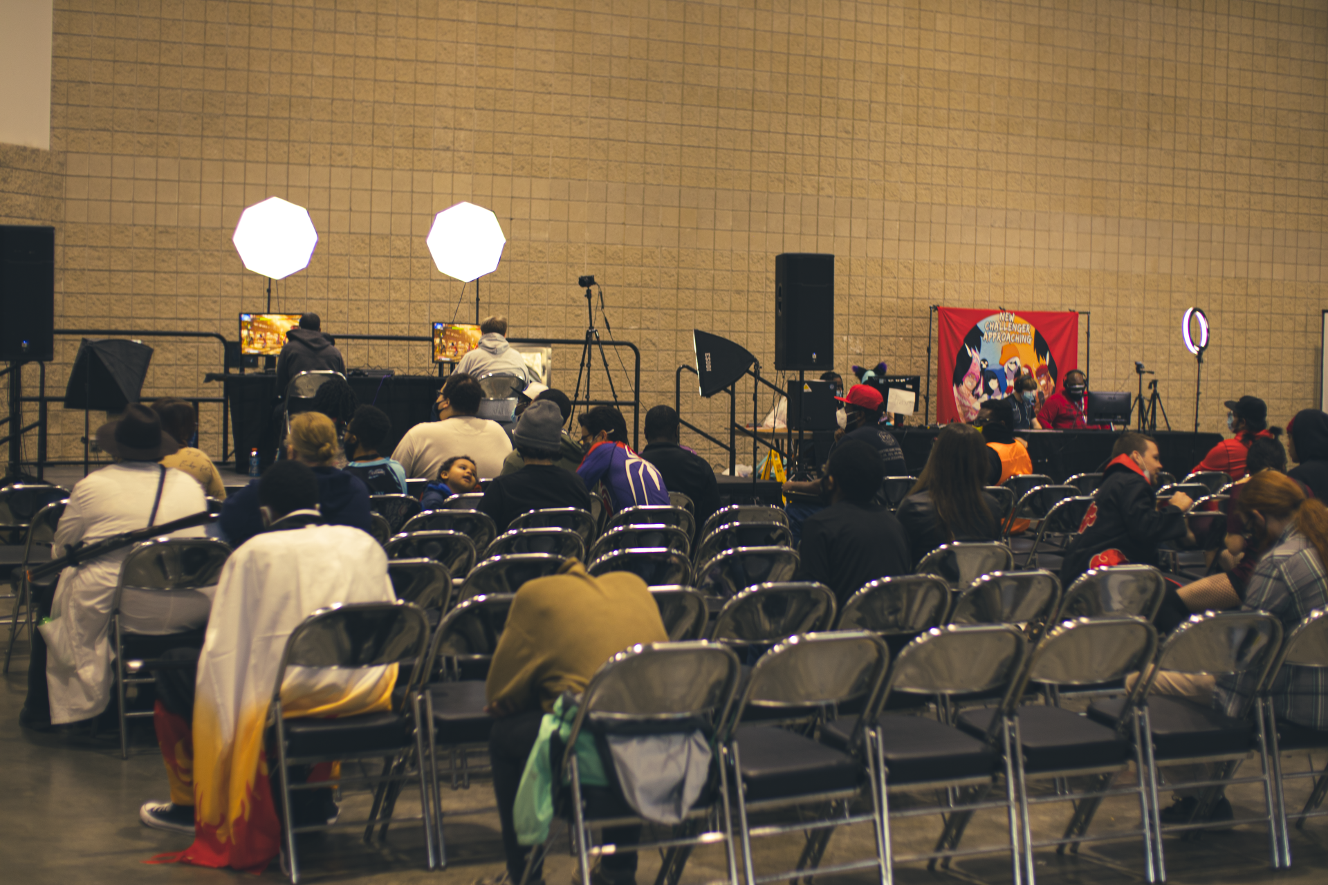 Audience at a panel discussion; speakers at front table. Room with beige walls, black chairs.
