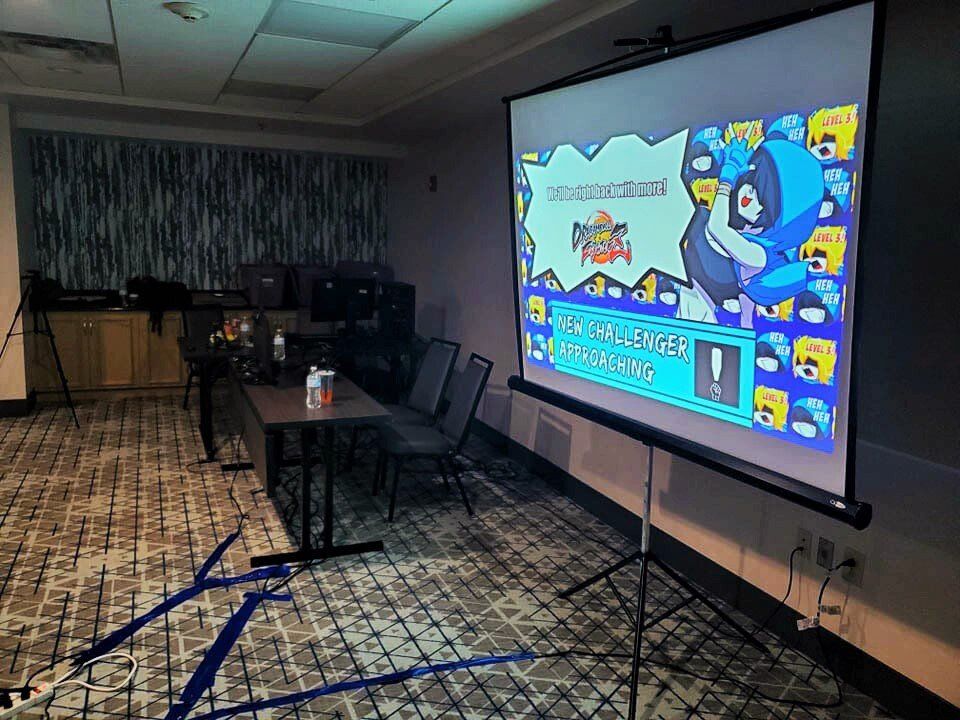 A projector displays a Mega Man game in a room with a table, chairs, and AV equipment.