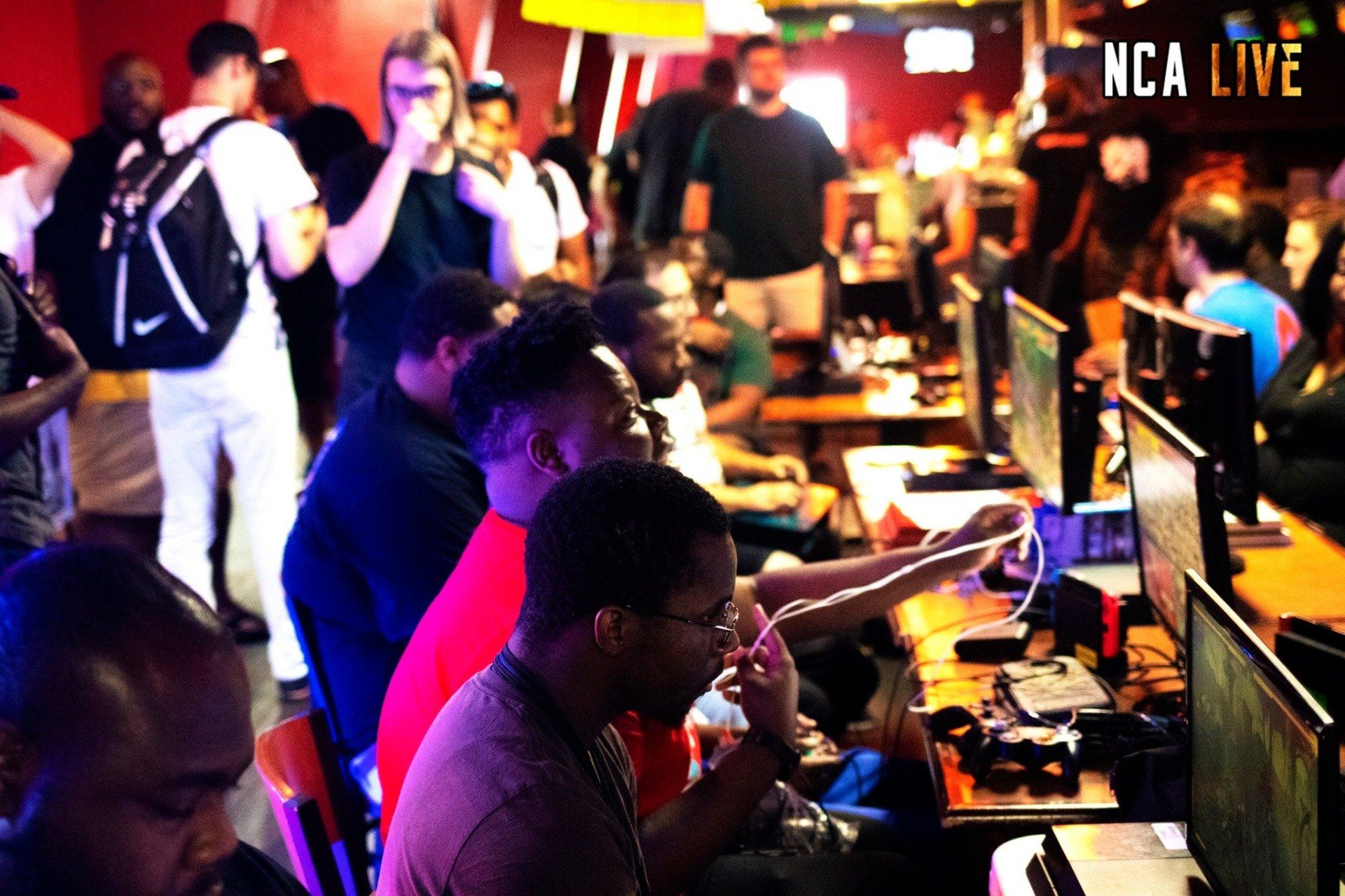 People at computers in a gaming competition, indoors. Many spectators watch from behind.
