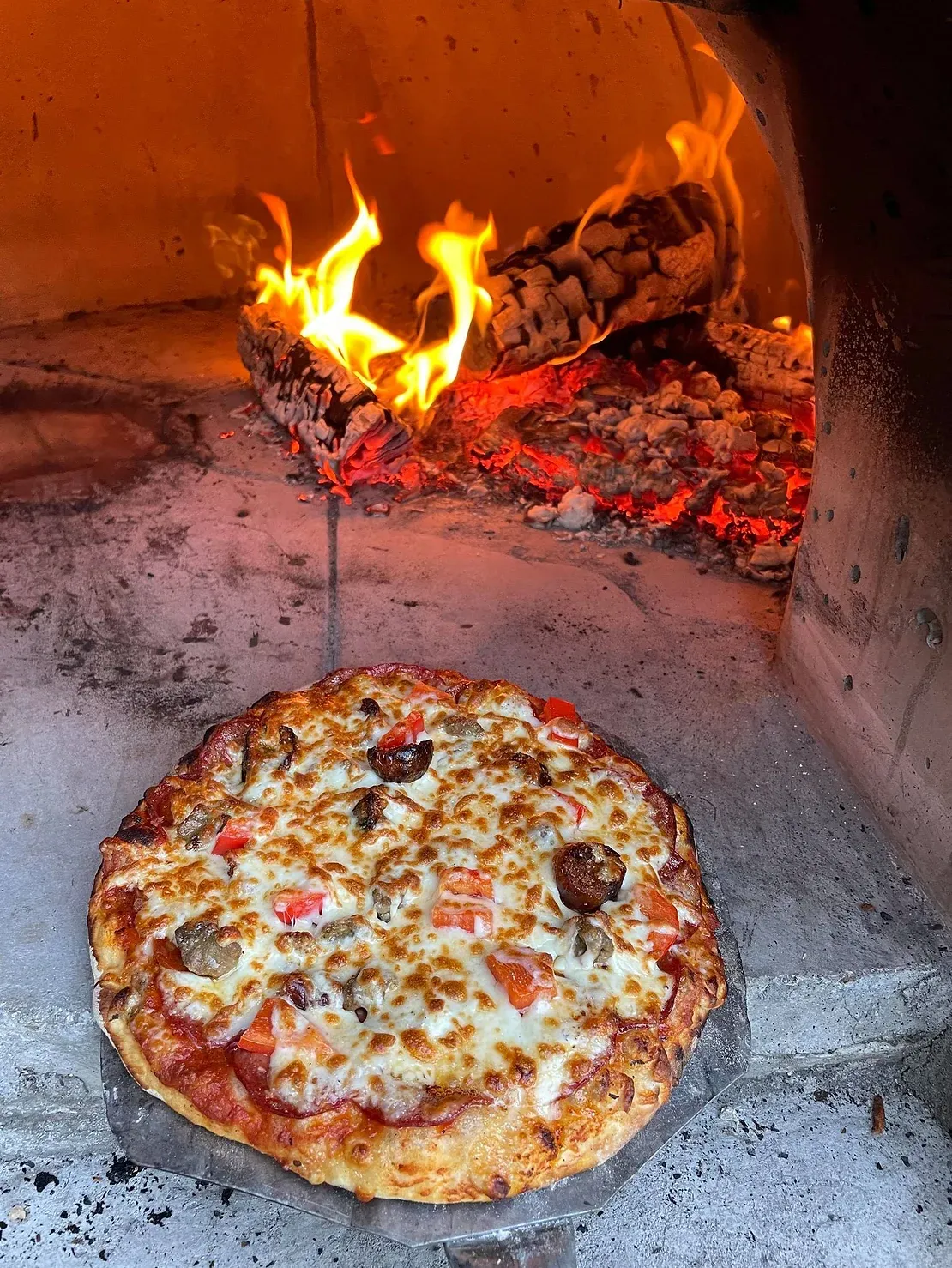 Cuisson de pizzas dans un four à bois avec des flammes en arrière-plan.