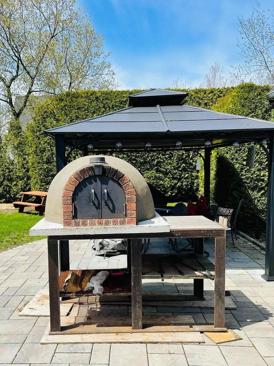 Four à pizza sur une terrasse en briques sous un kiosque, cadre extérieur ensoleillé.