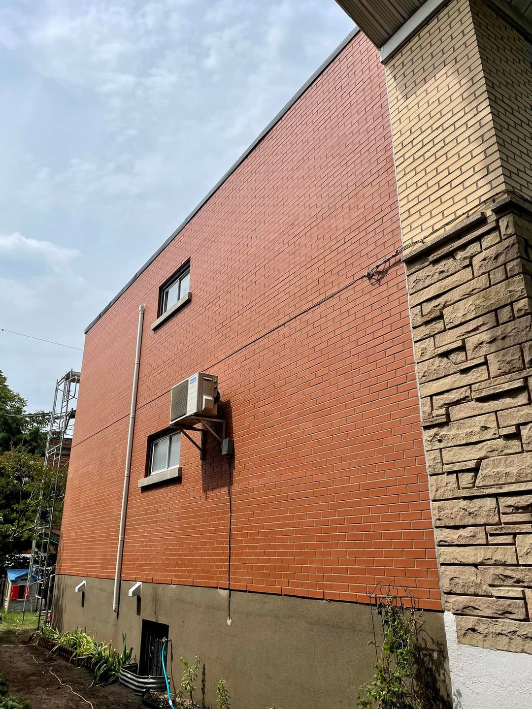 Bâtiment en briques avec deux fenêtres et un climatiseur ; ciel nuageux.