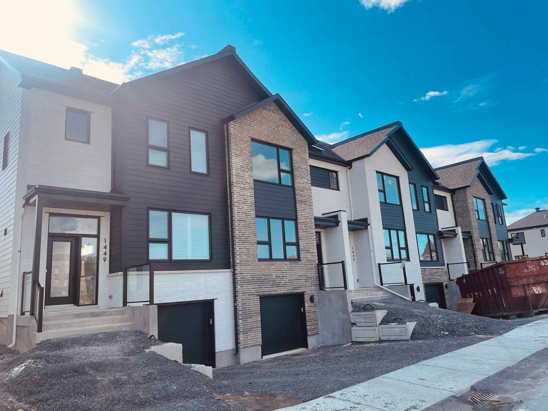 Rangée de maisons de ville modernes aux façades contrastées noires, beiges et blanches se détachant sur un ciel bleu.