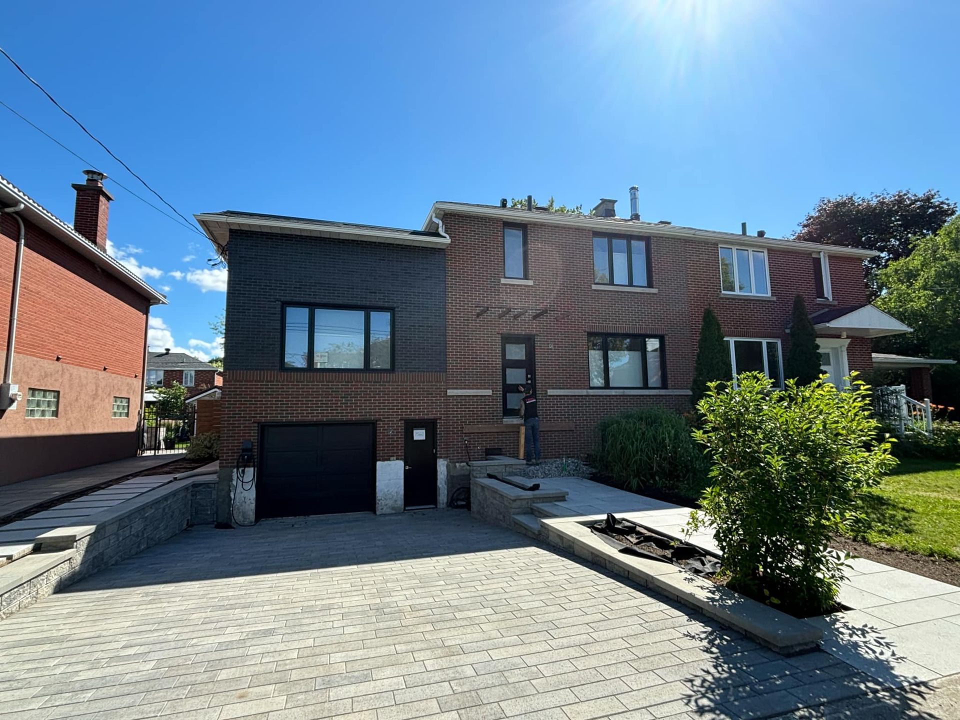 Maison en briques avec bardage gris, allée, garage et petite cour avant par une journée ensoleillée.