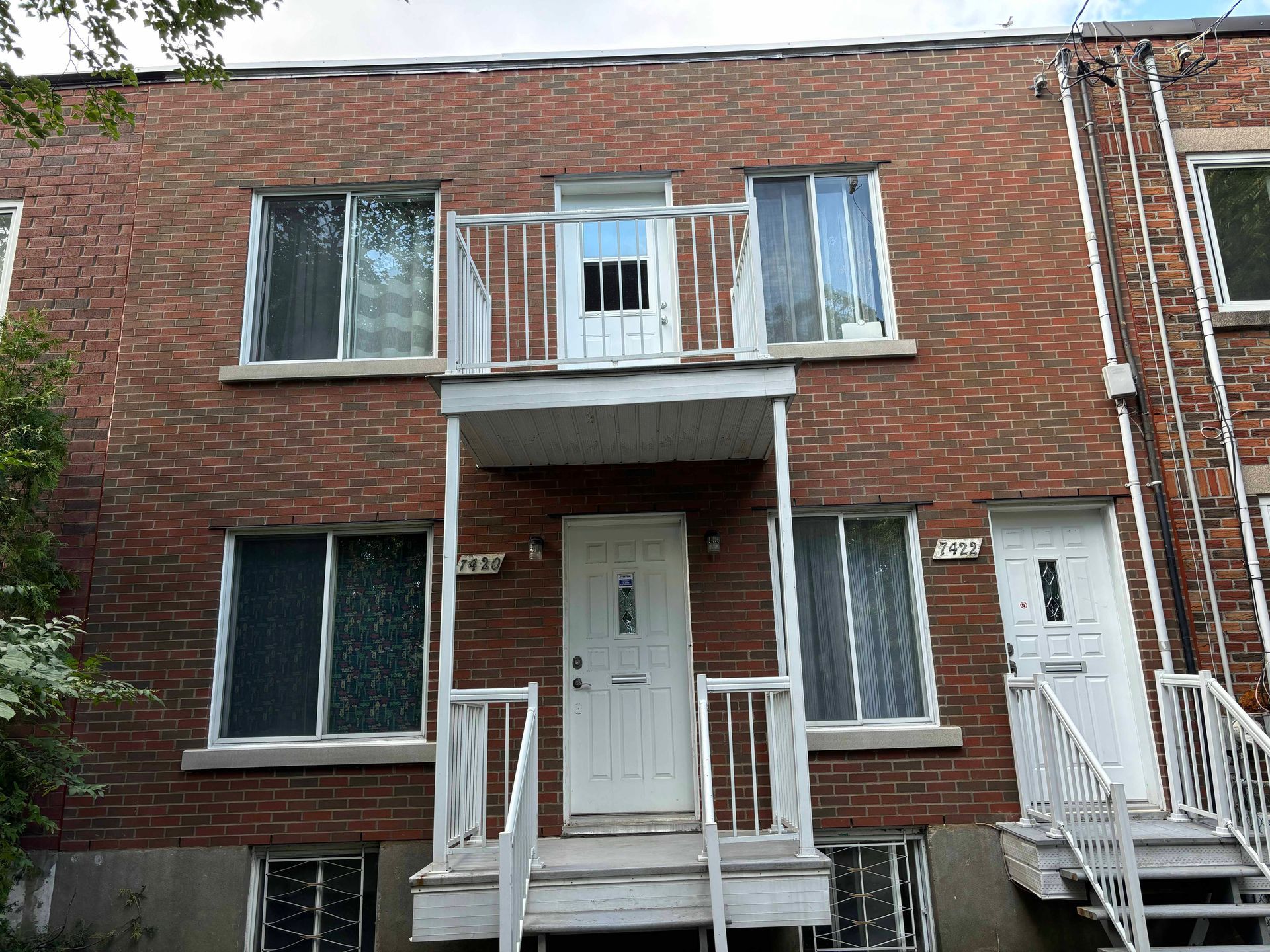Immeuble en briques rouges avec portes blanches et petit balcon. Fenêtres visibles aux deux étages.