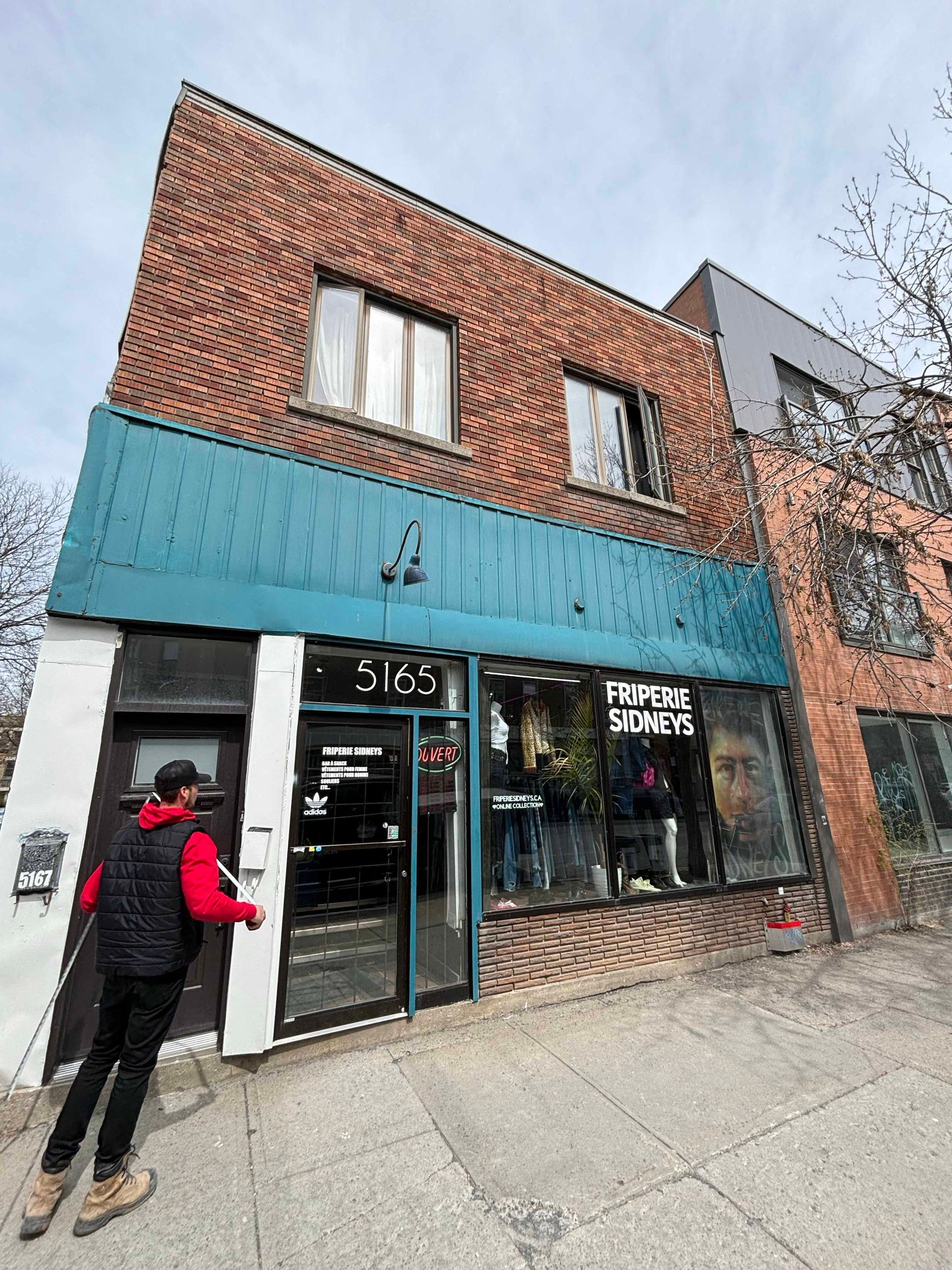 Une personne entre dans une librairie de bandes dessinées à la façade turquoise ; bâtiment en briques rouges.