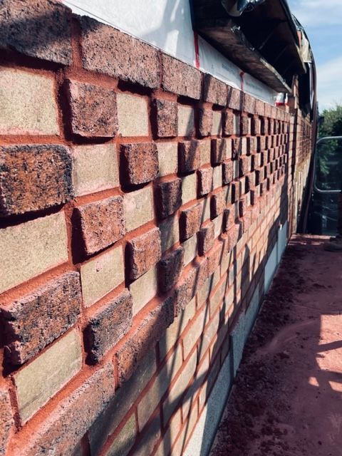 Mur de briques avec briques saillantes alternées, mortier rouge, extérieur ensoleillé.