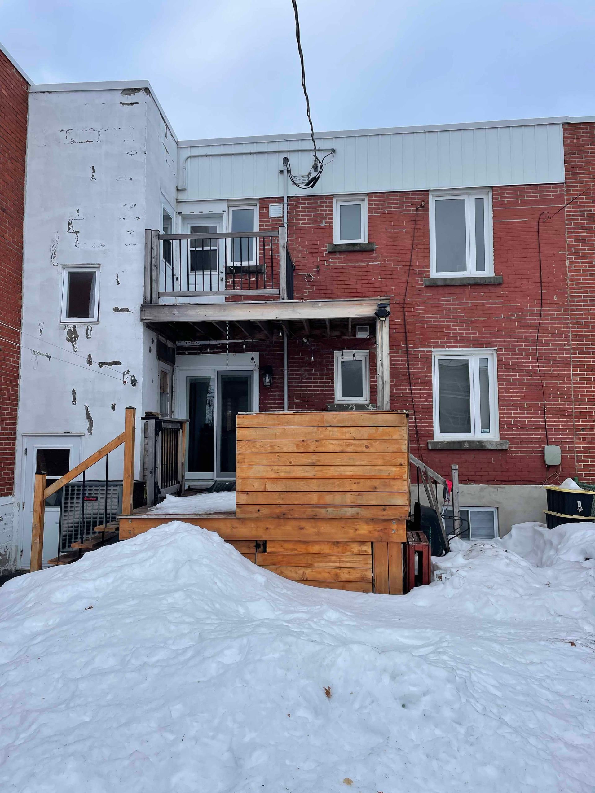 Arrière d'un bâtiment en briques avec une terrasse en bois et une cour enneigée.