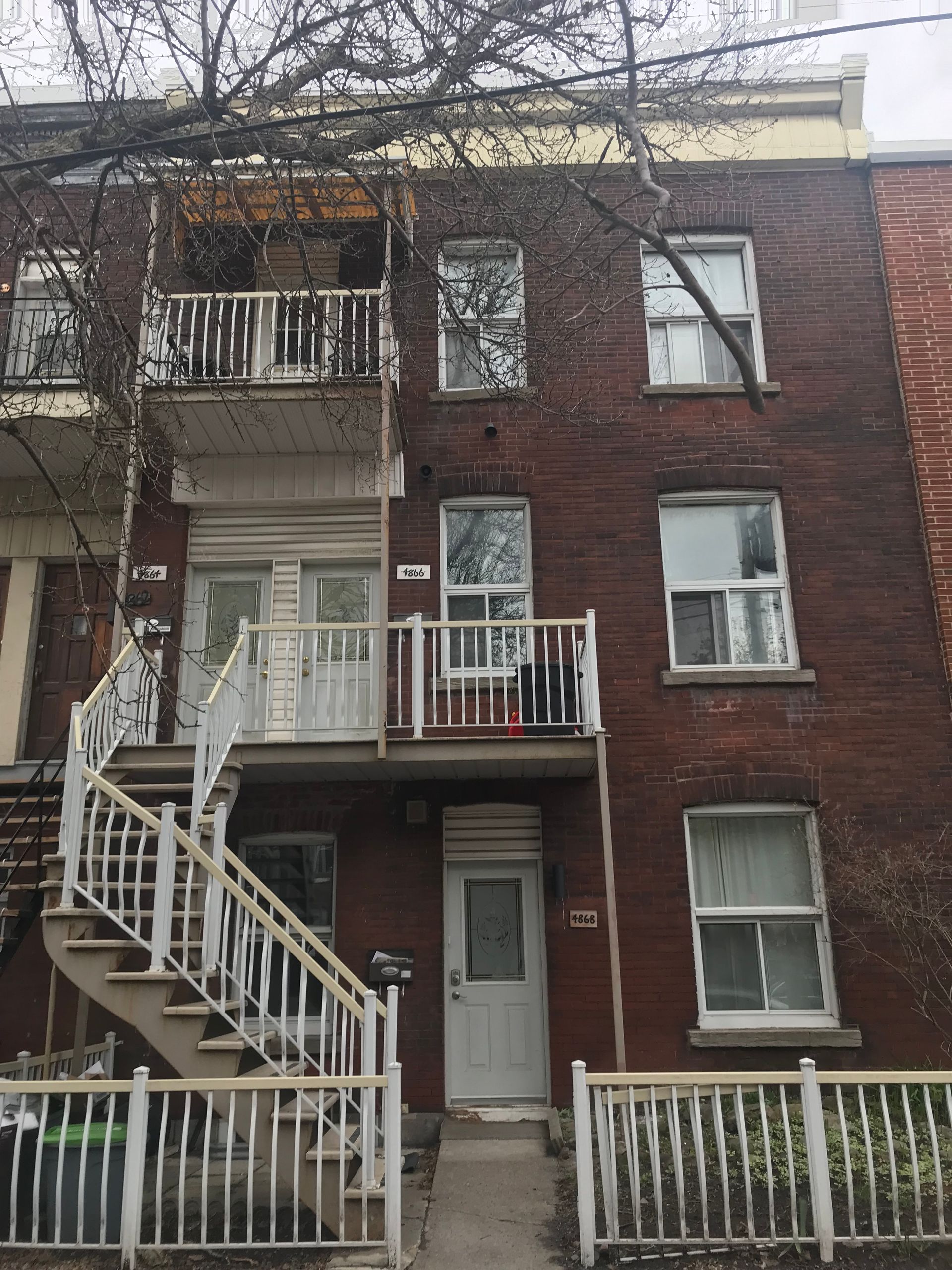 Immeuble d'appartements en briques avec escaliers extérieurs et balcons ; branches d'arbres dénudées au-dessus.