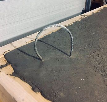 Boucle métallique encastrée dans du béton frais sur une armature en bois.