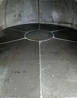À l'intérieur d'un four en pierre sombre et incurvé. Sol en pierre sombre divisé en sections par des lignes.