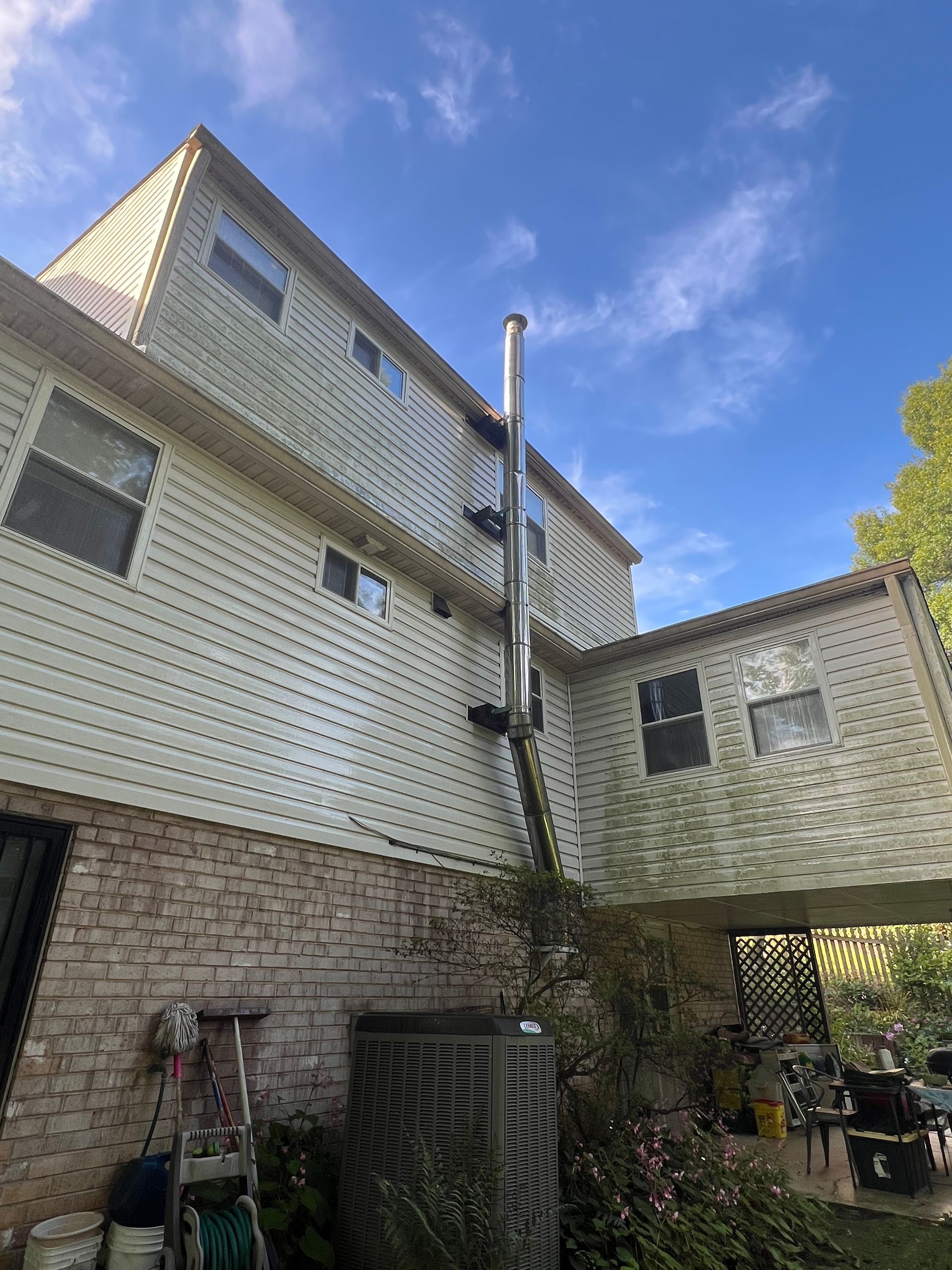 Exterior of a house with a tall, silver chimney attached to the side, blue sky.