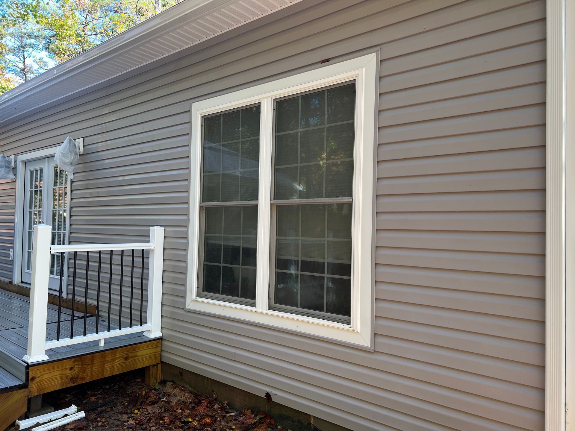 Gray house siding with a white-framed window. A small deck with a black railing is to the left.