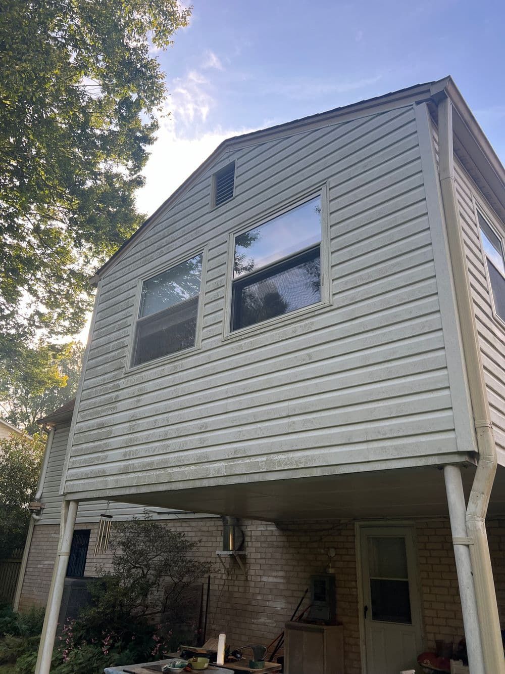 Two-story house with light siding and windows, viewed from below with some trees and blue sky.