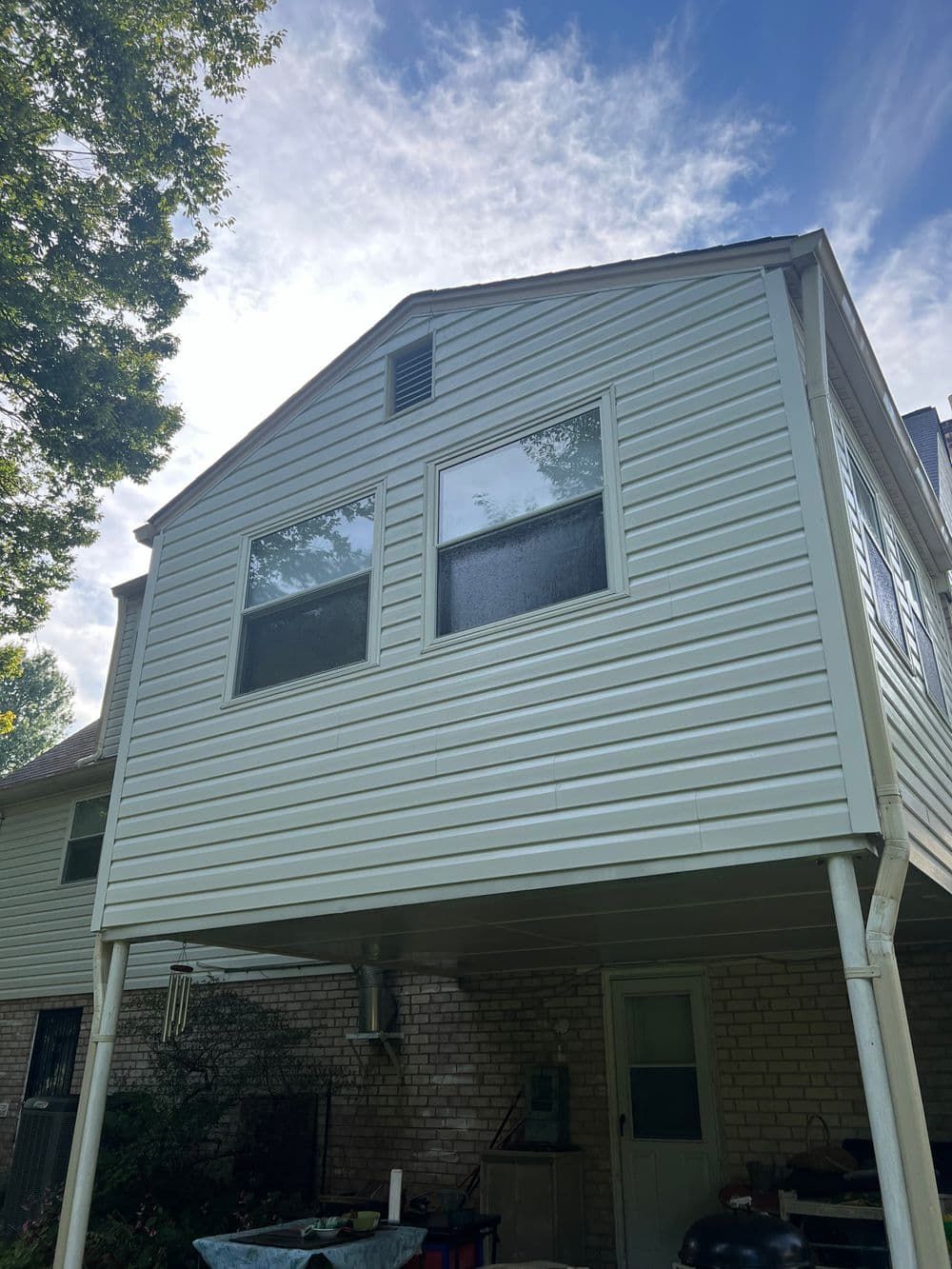 Beige vinyl-sided house with a porch underneath, two windows, and a cloudy sky.