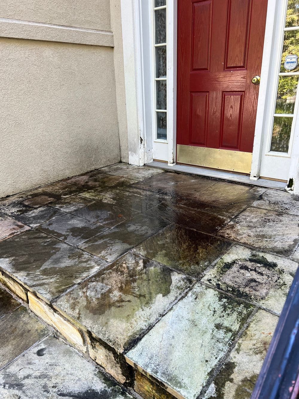 Stone porch at a house entrance with dark stains, red door, white trim, and a step.