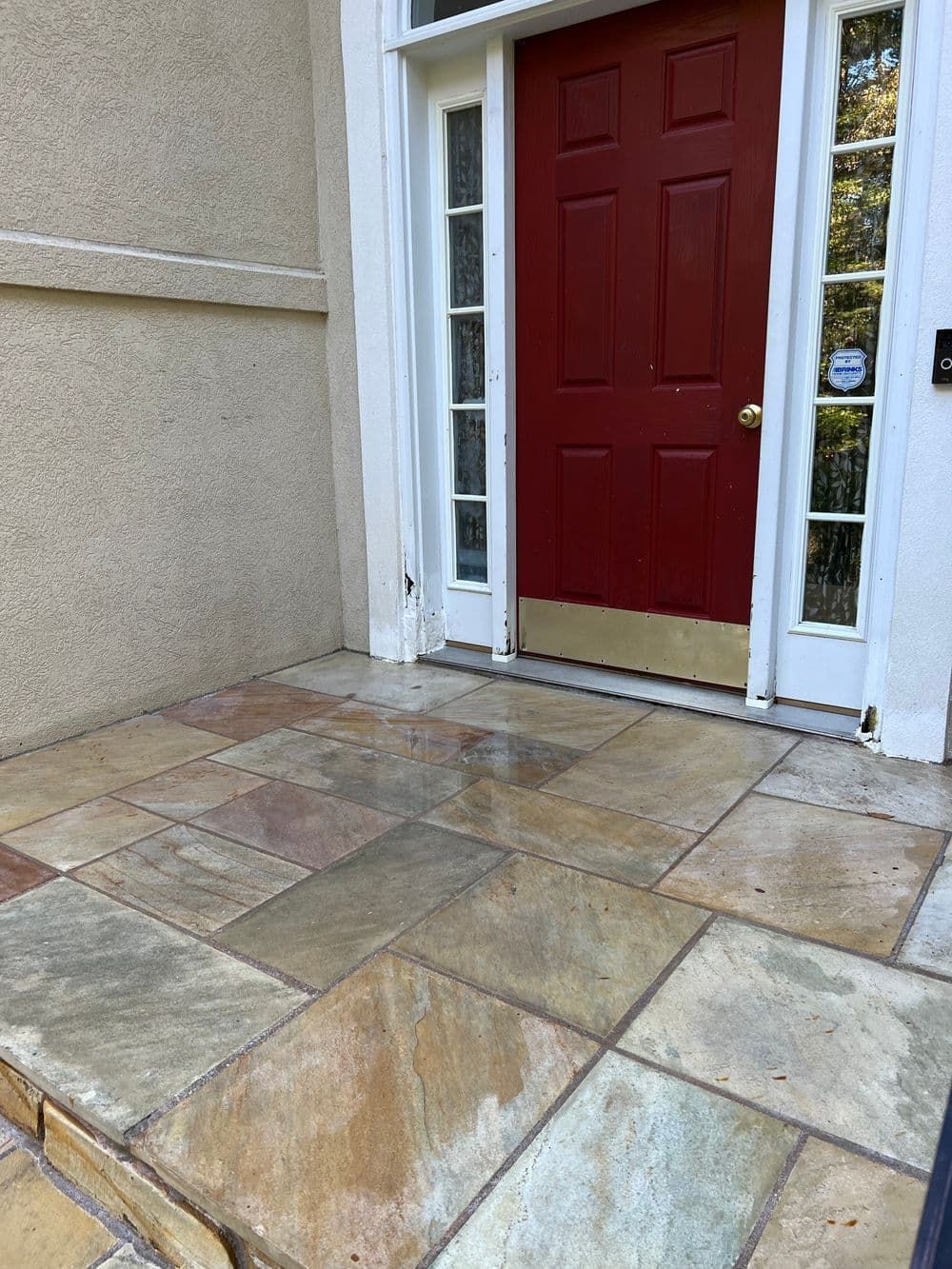 Stone tiled front porch with a red door and white trim.