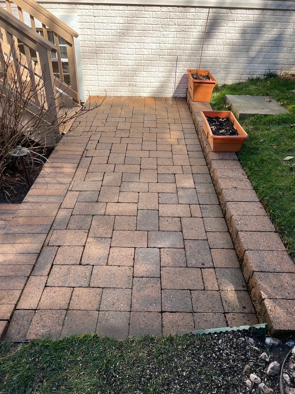 Brick pathway leading to wooden deck, flanked by grass and planter boxes.