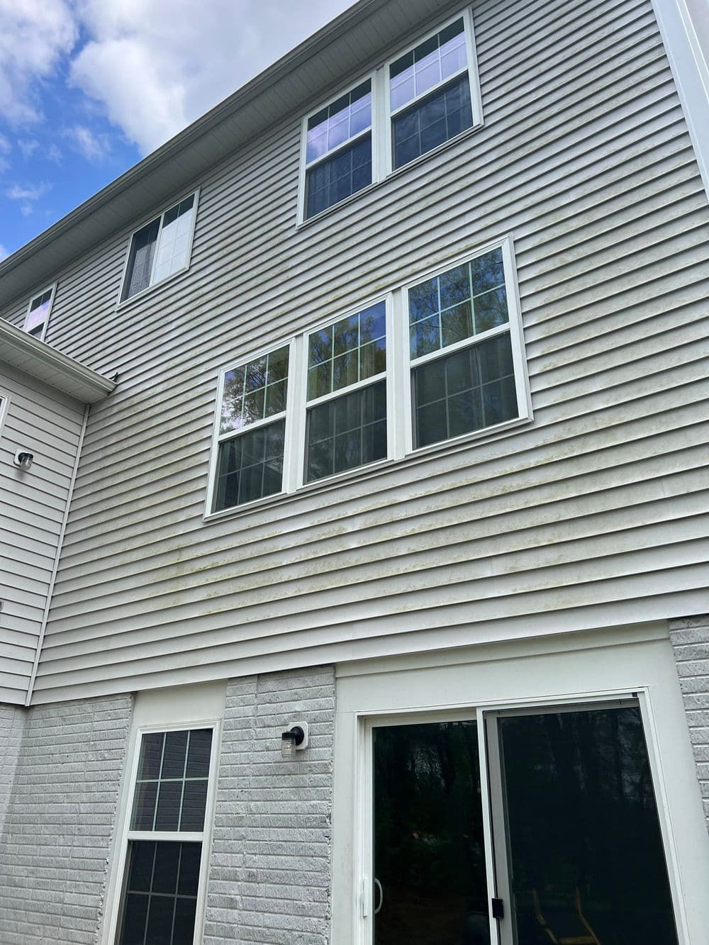 Gray house exterior with windows, some covered in grime, and a sliding glass door.