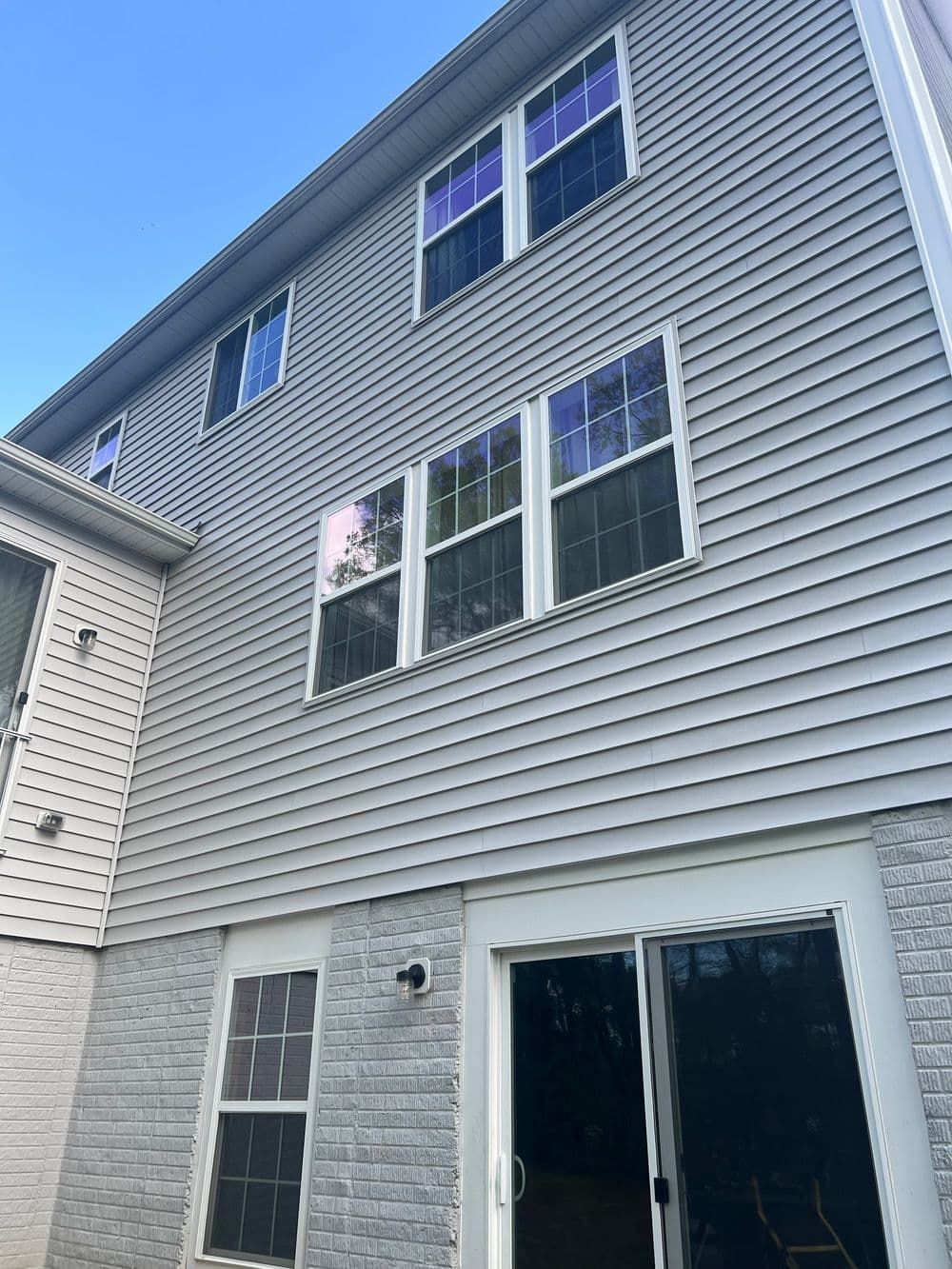 Exterior of a two-story house with gray siding, white trim, and a sliding glass door.