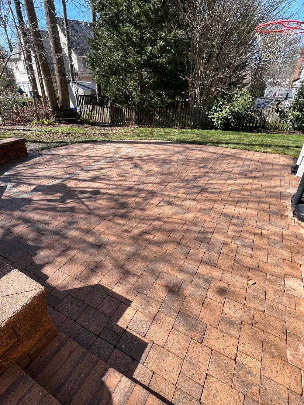 Brick patio in backyard with grass and trees.