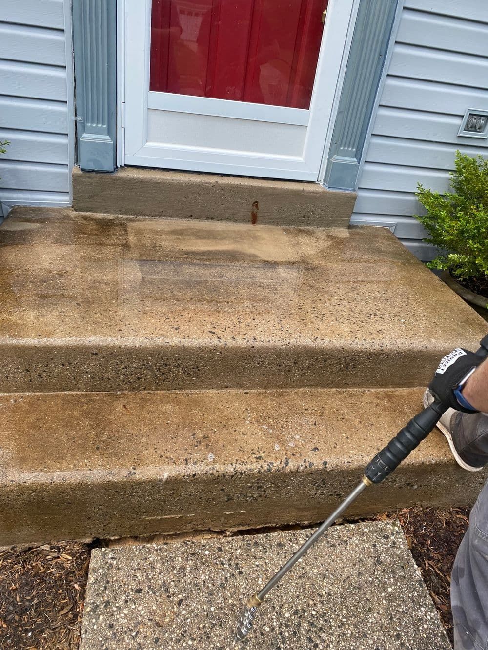 Person power washing concrete steps in front of a house. Red door, gray trim.