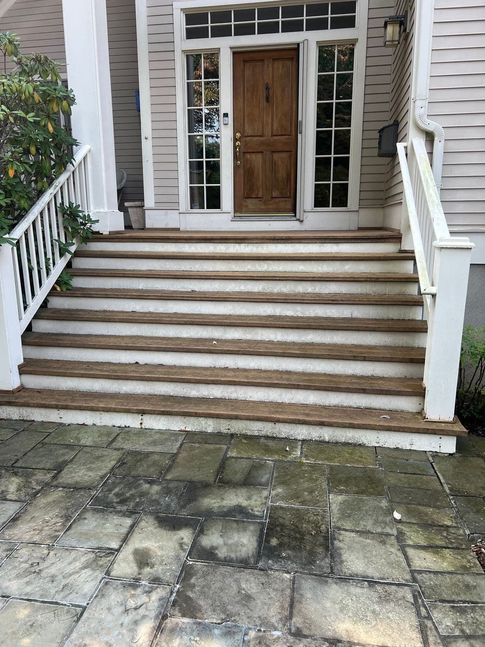 Exterior view of a house with wooden steps leading to a front door. Gray stone patio in the foreground.