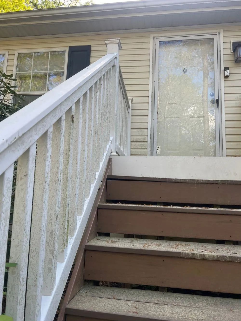 Wooden steps leading up to a front door with a screen door; white railing on the left.