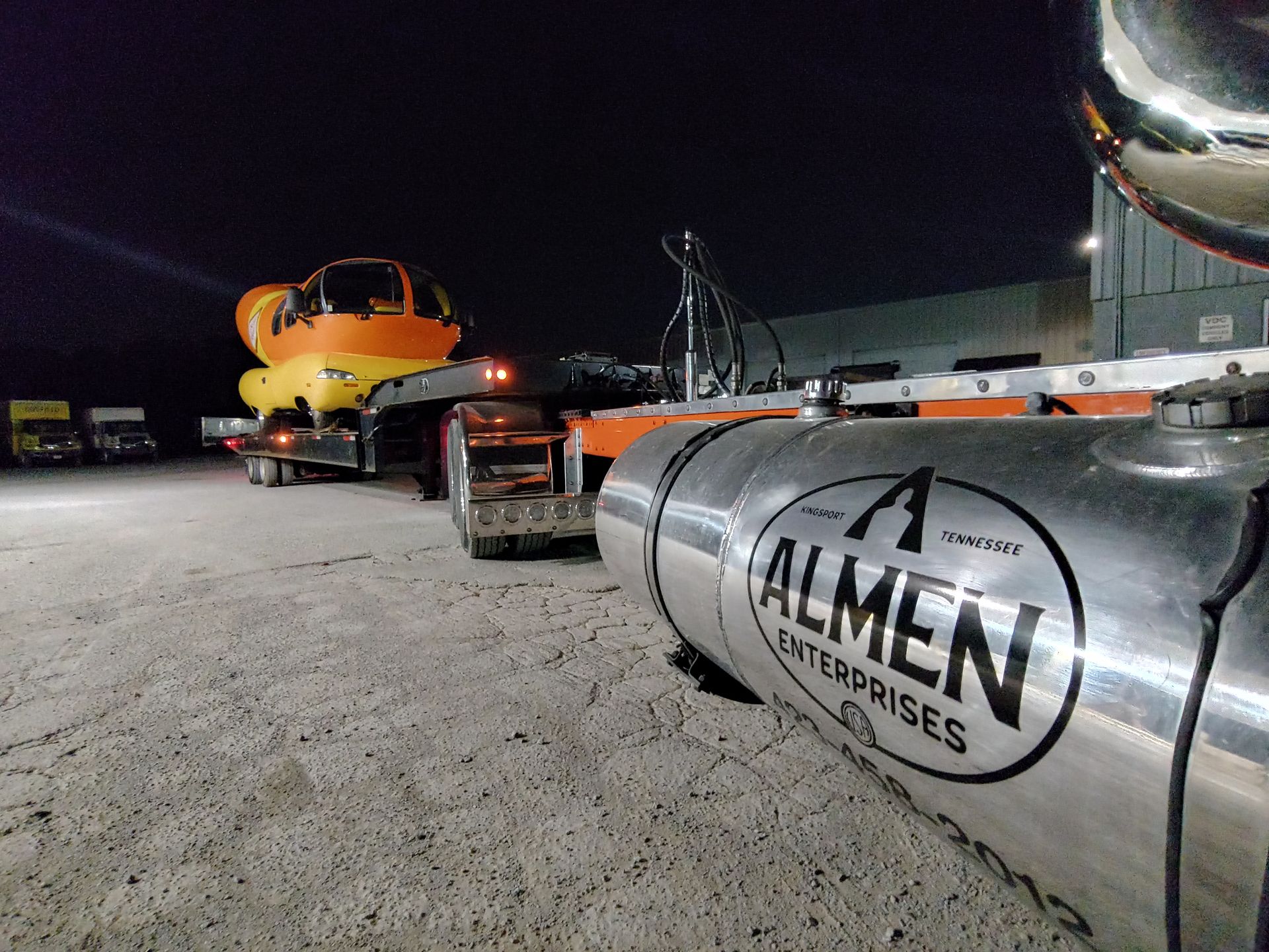 A truck hauling an orange vehicle at night | Almen Enterprises