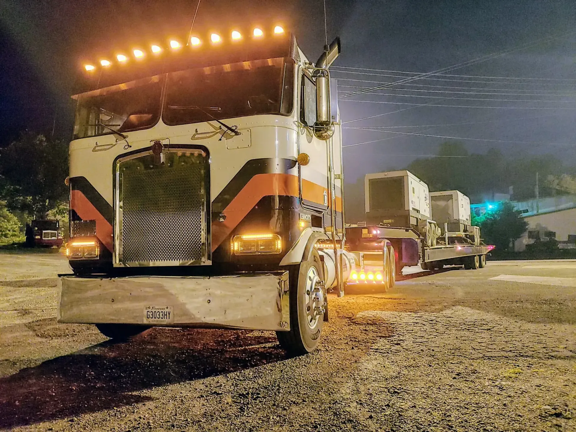 A large semi truck is parked in a gravel lot at night.