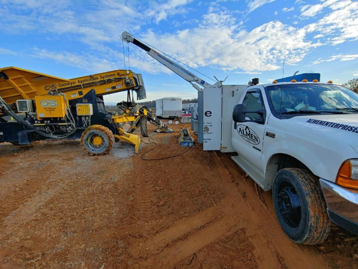 A white truck is parked in the dirt next to a crane.