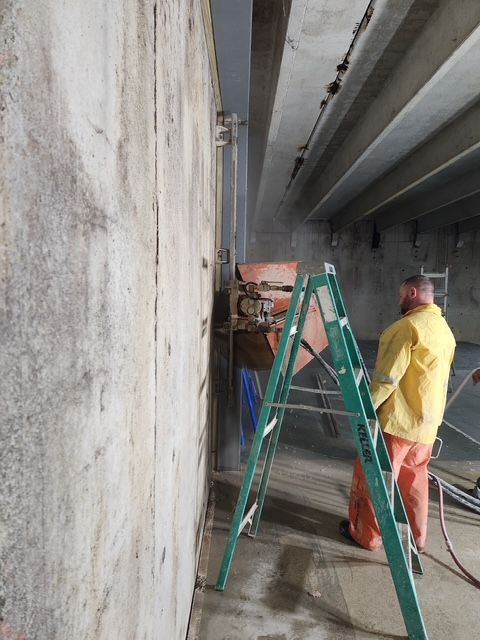 A man in a yellow jacket is standing next to a green ladder.