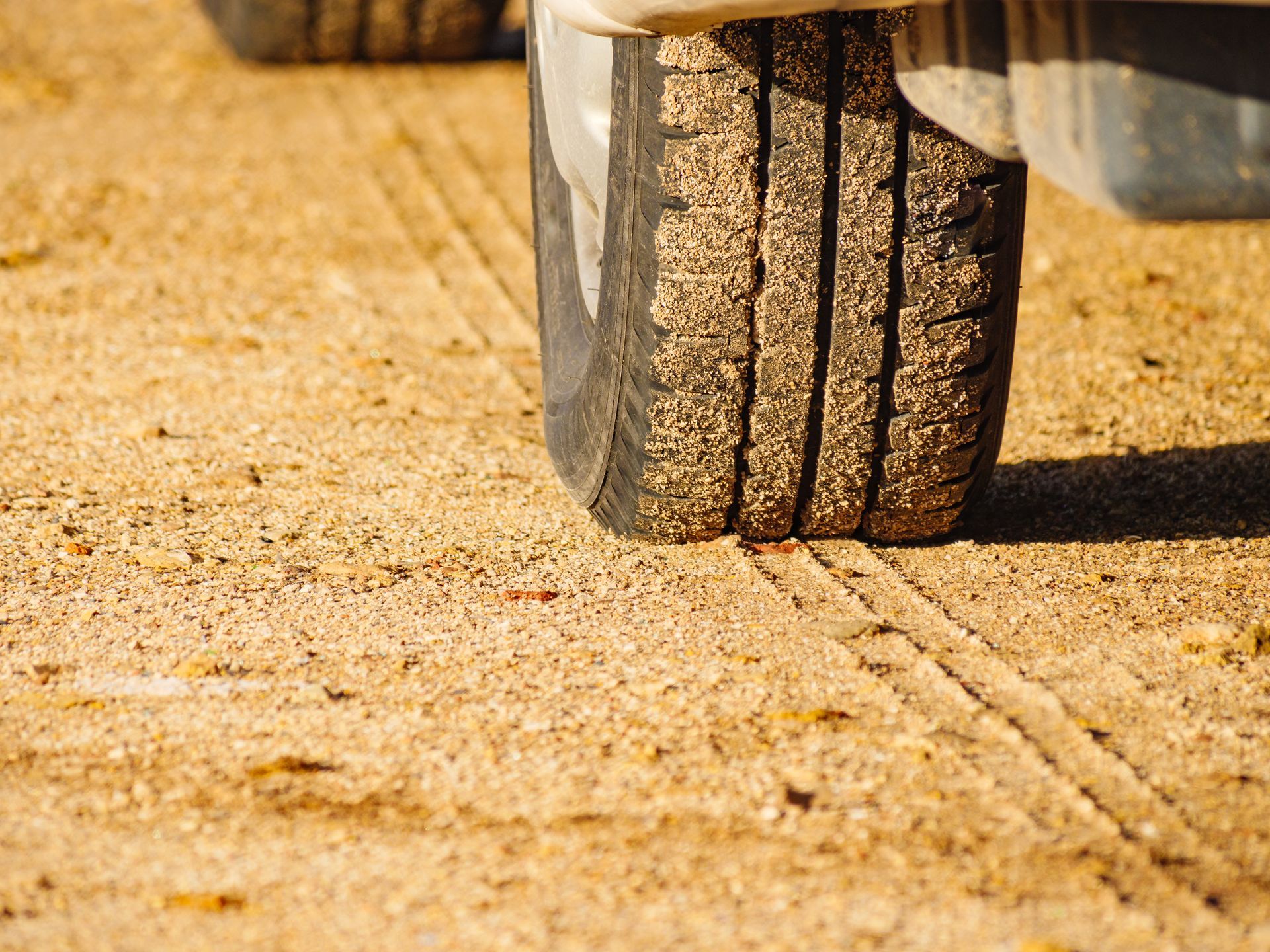 Close-up of a vehicle tire on sandy ground, leaving a track in the dirt.