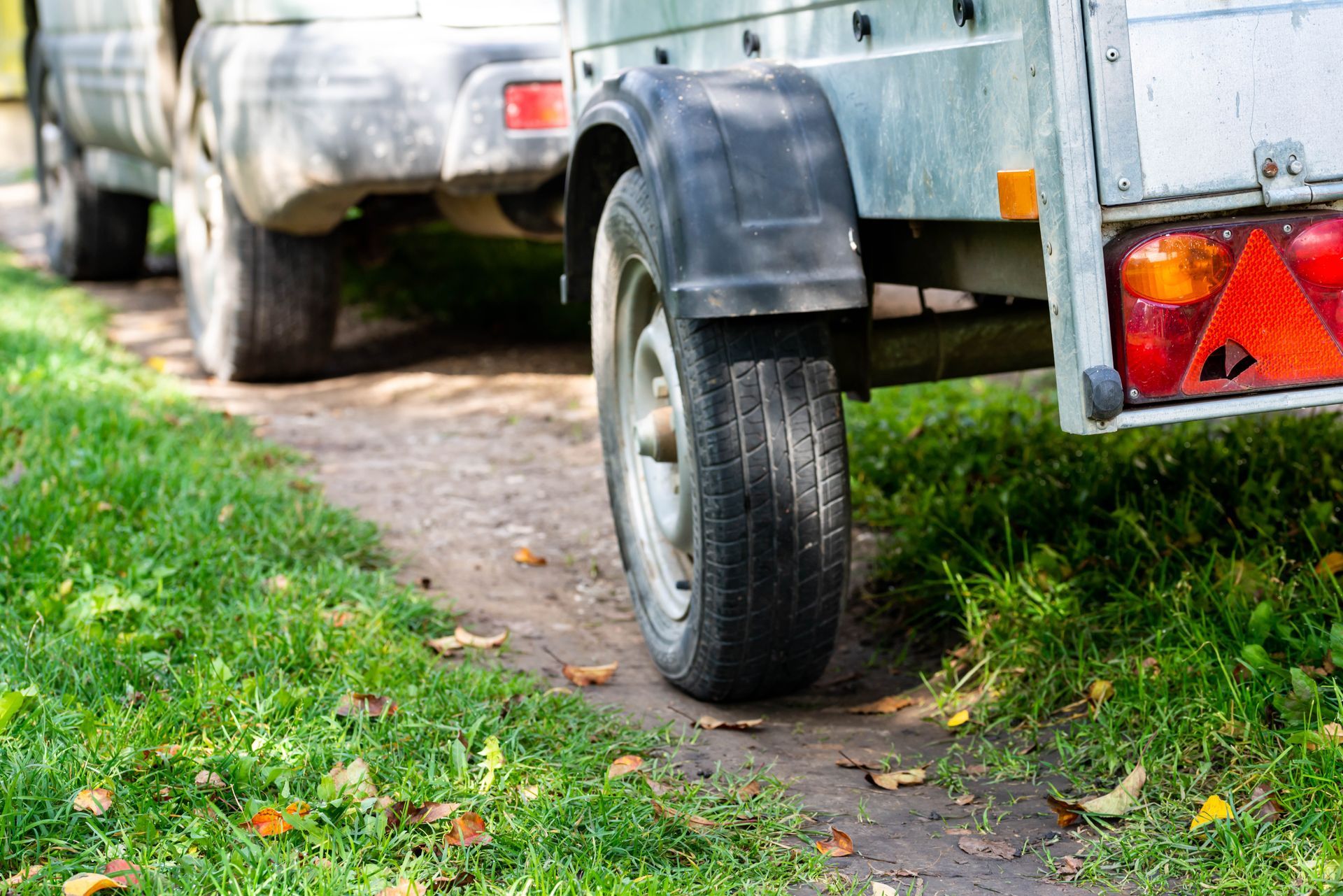 Trailer parked on a grassy path, with a car visible behind it.