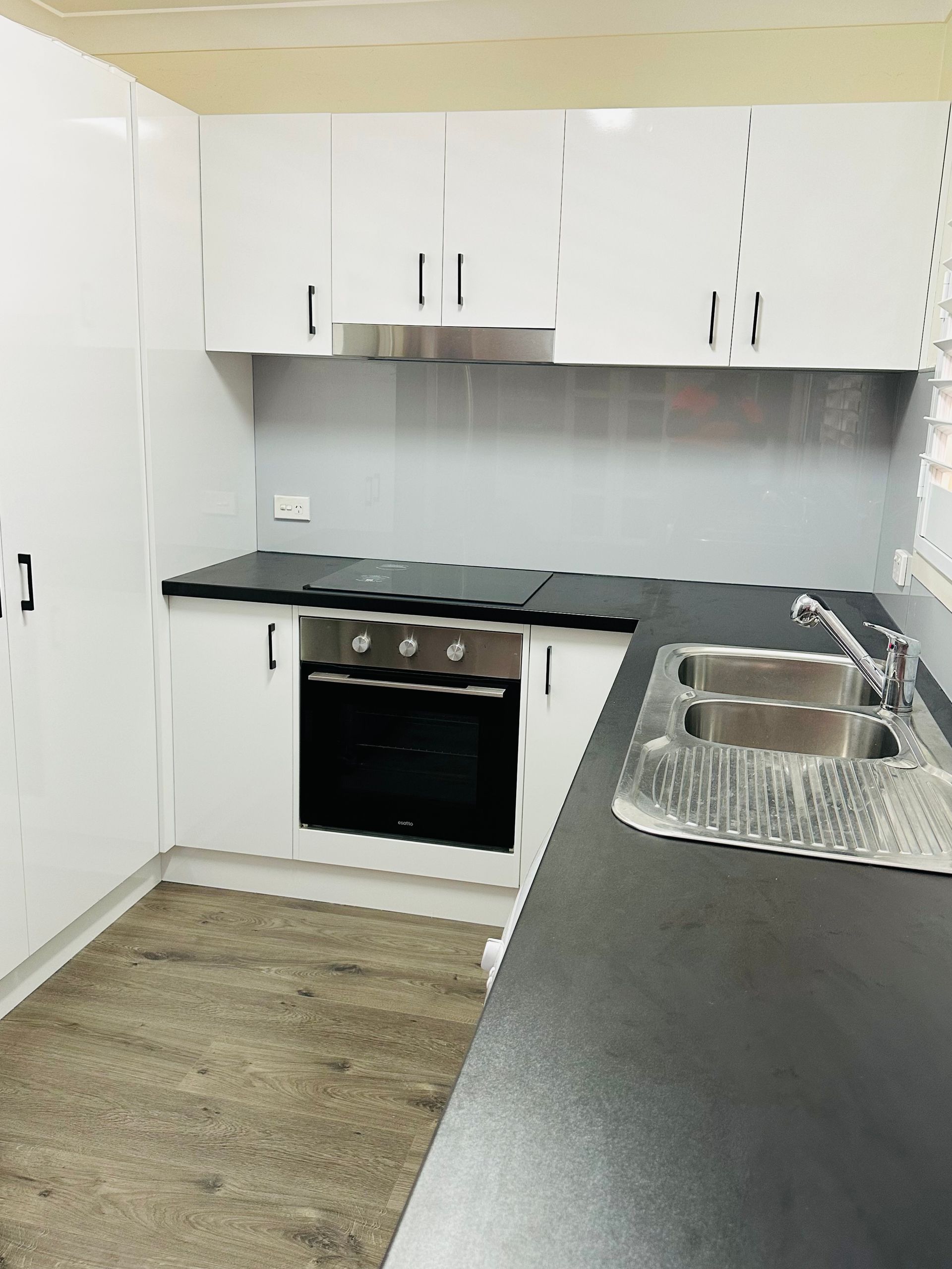 A Kitchen With White Cabinets, Black Counter Tops, and a Stove Top Oven — Nyon Shopfitters in Morisset, NSW