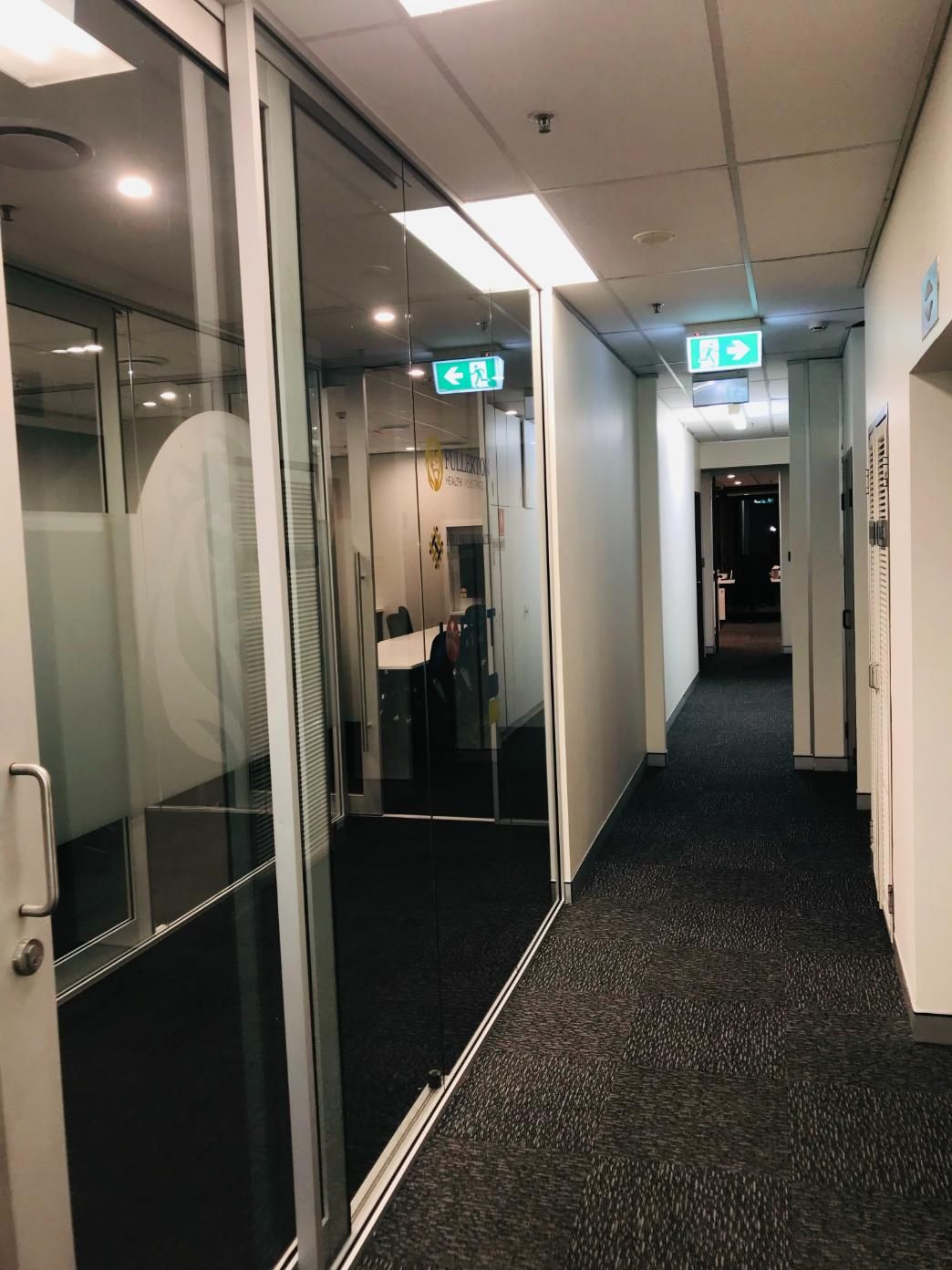 A Long Hallway in an Office Building With a Green Exit Sign — Nyon Shopfitters in Morisset, NSW