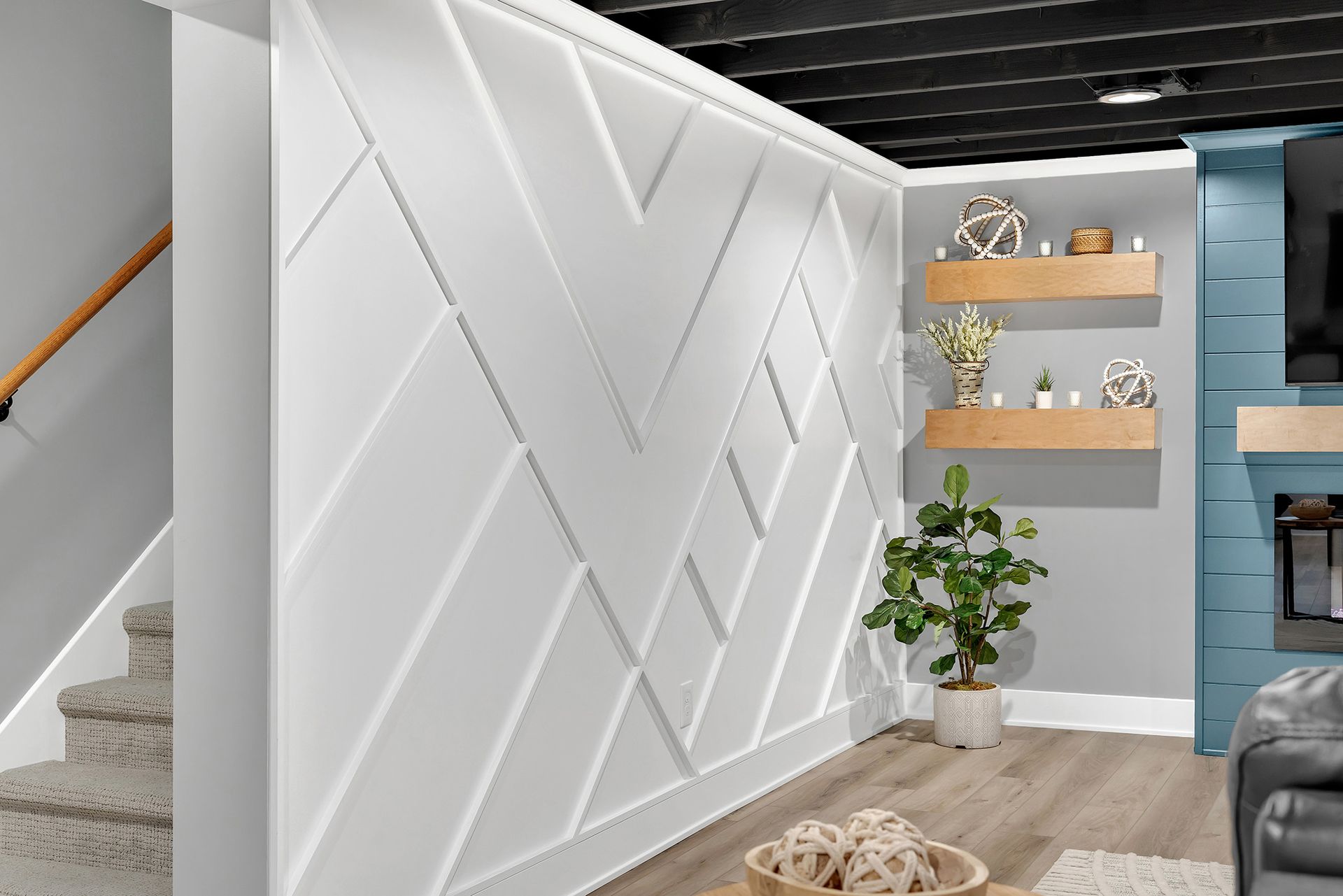 A living room with a staircase and an accent wall with a geometric pattern.