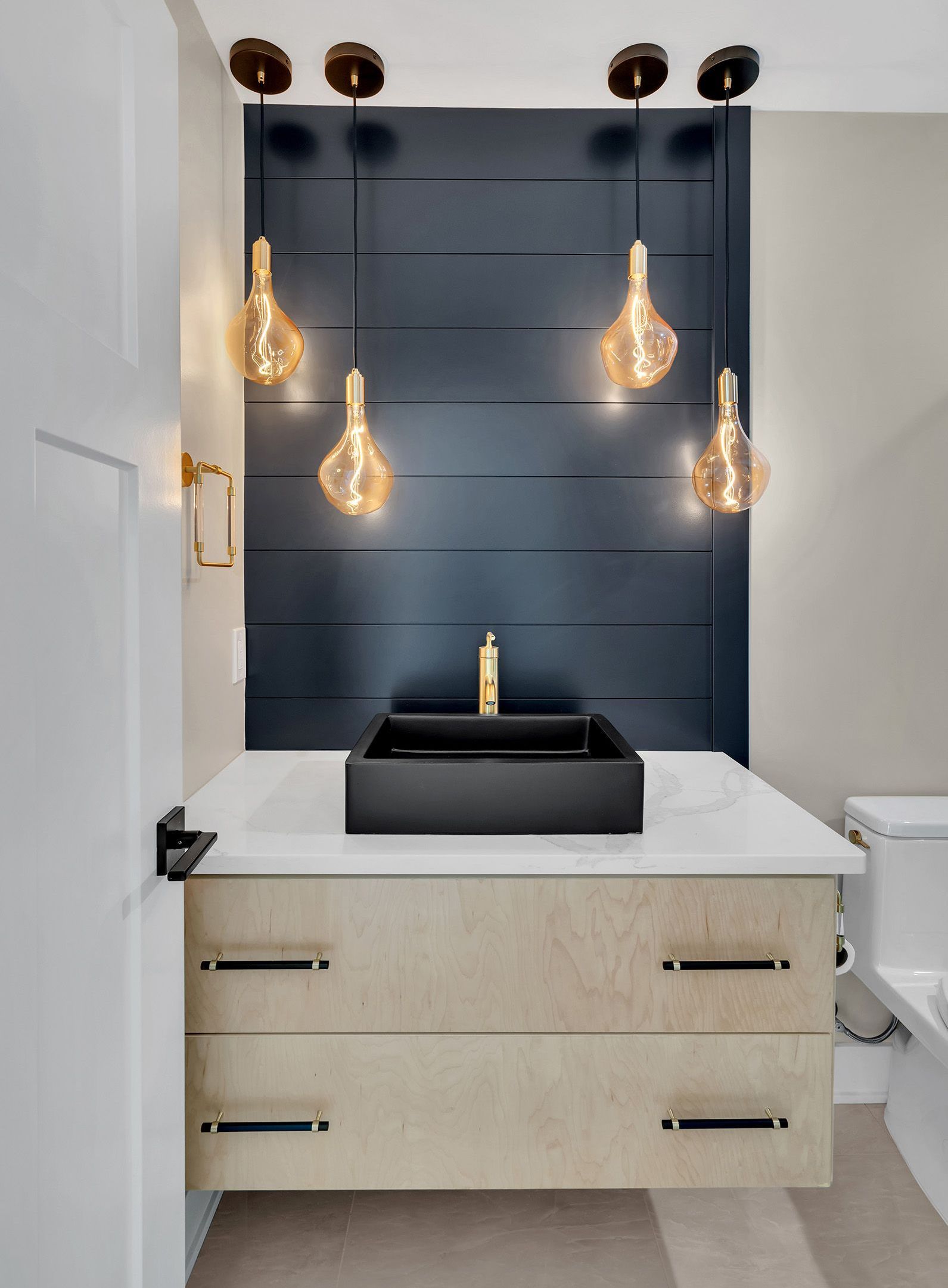 A bathroom with a sink , toilet , and lights hanging from the ceiling.