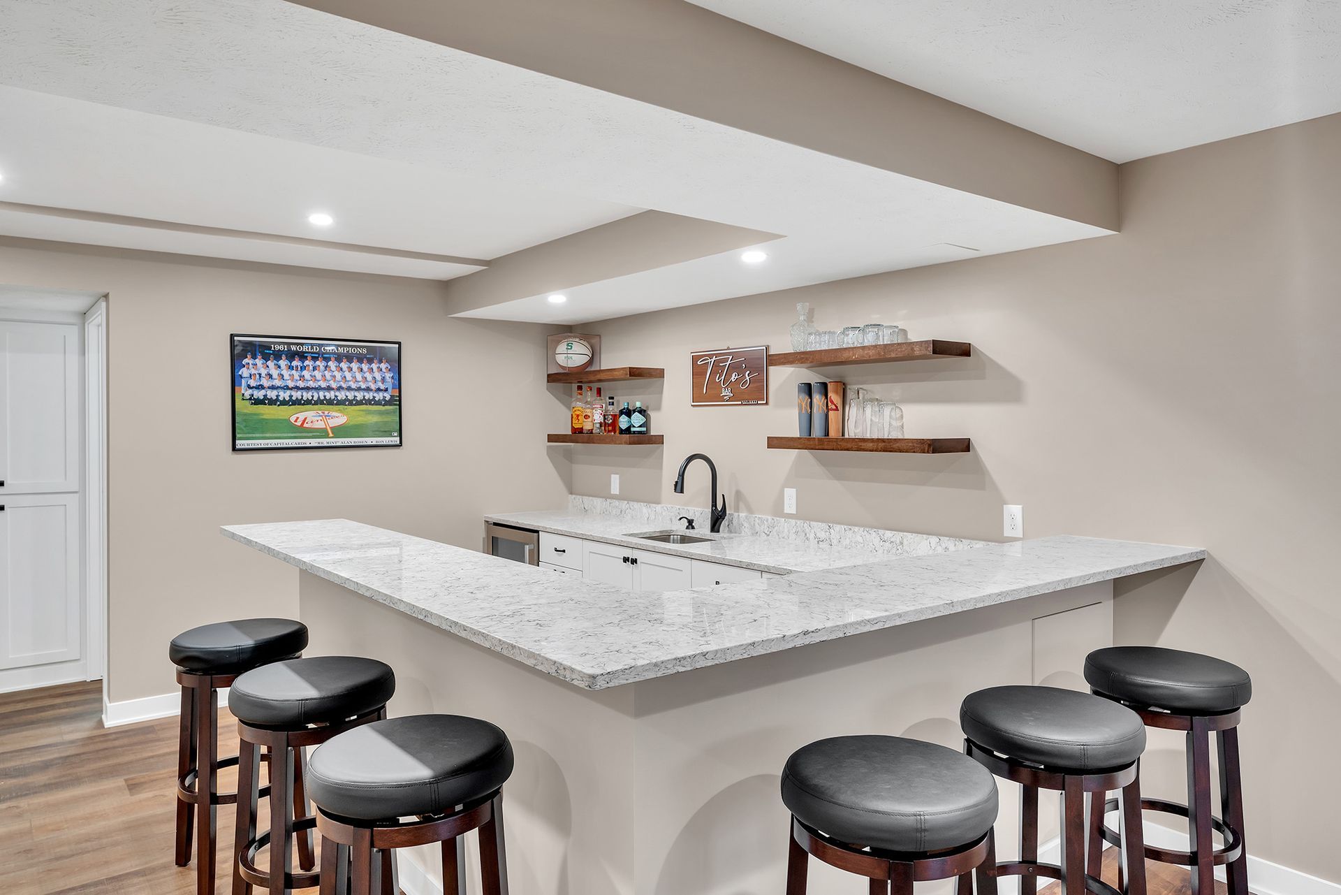 A kitchenette bar in a basement with stools and a sink.
